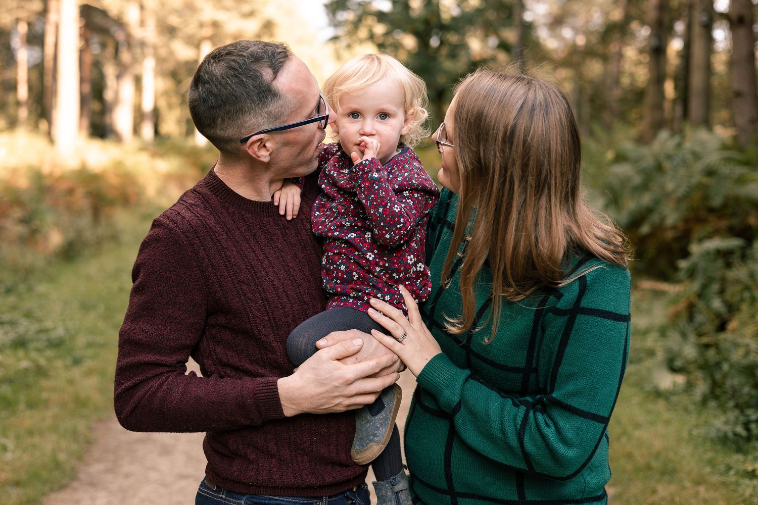 Outdoor Family Photoshoot in a wood near Pocklington, Mum and Dad kiss daughters cheeks whilst she looks at the camera.
