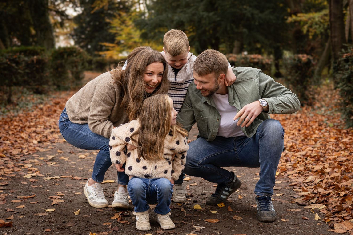 Family sharing intimate moment on autumn path covered in fallen leaves.