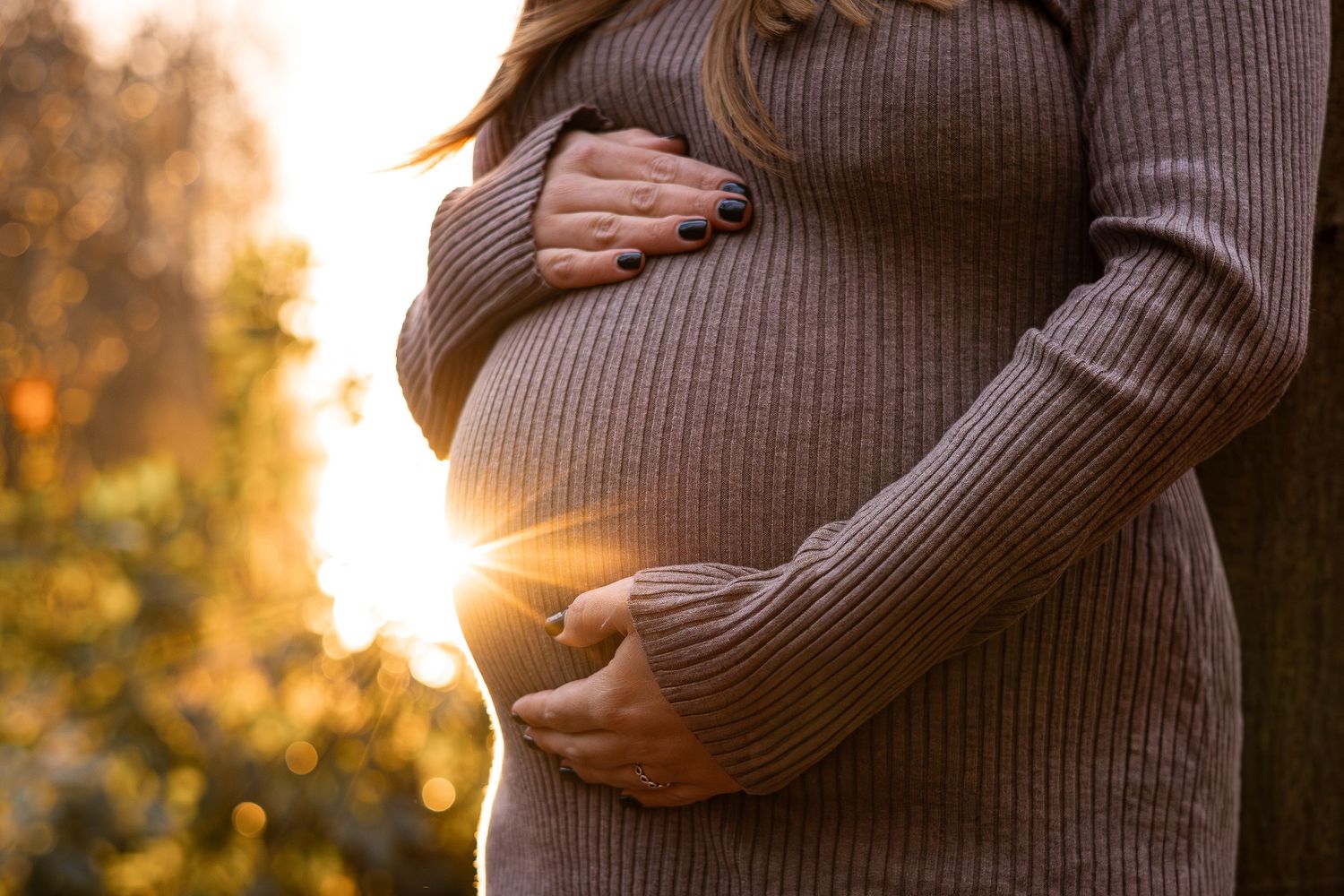 Silhouette of pregnant belly against sunset while wearing brown sweater.