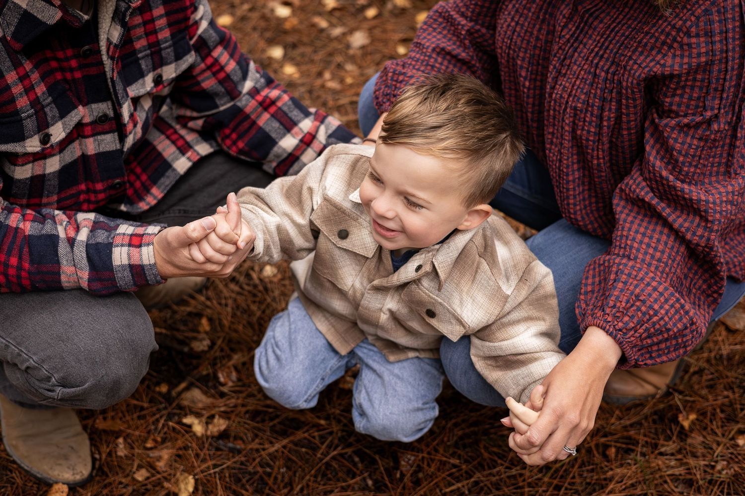 Autumn mini family photoshoot taken in Yorkshire with a cheeky little boy smiling whilst holding his parents hands.