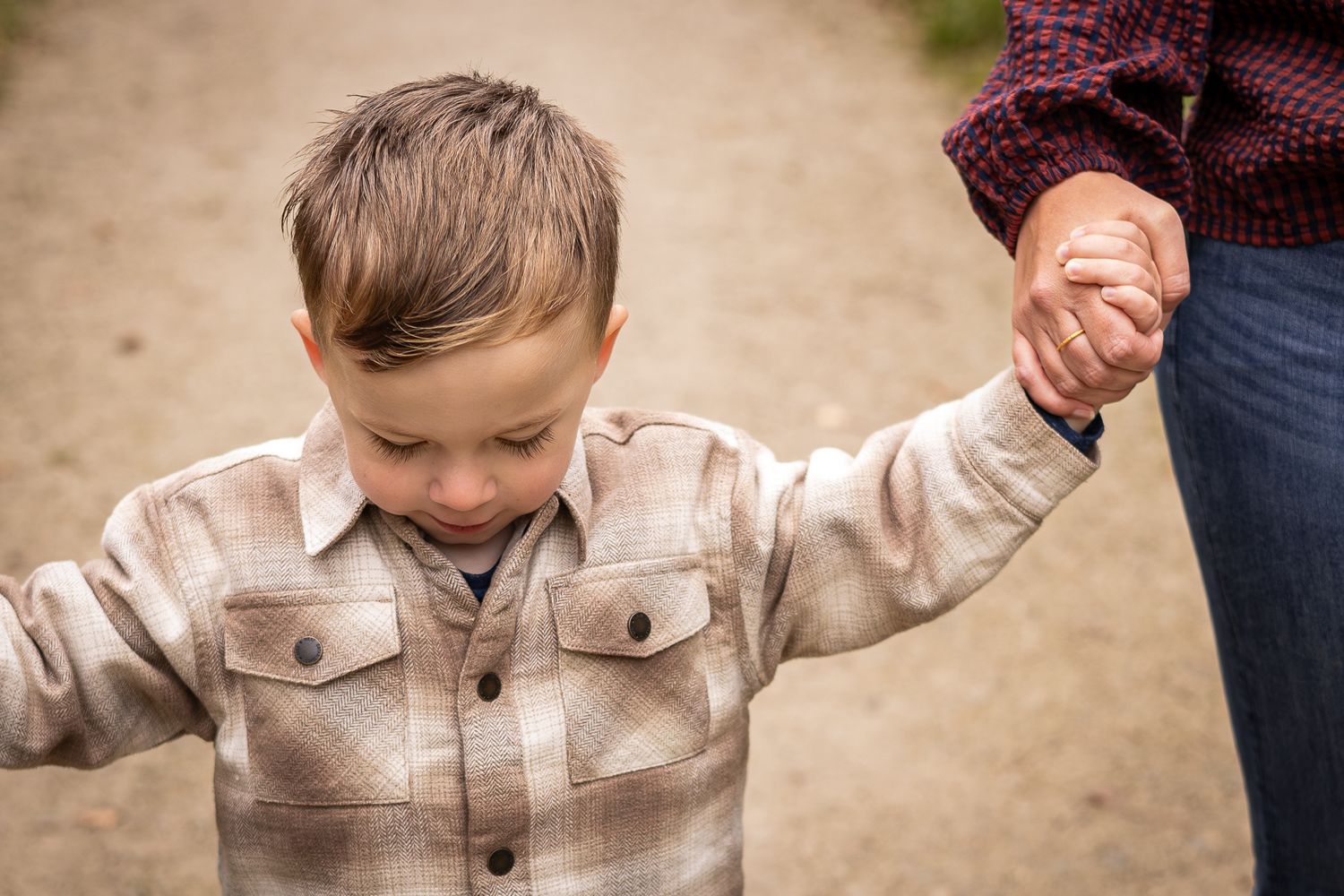 A small child in a plaid jacket walking while holding hands outdoors.