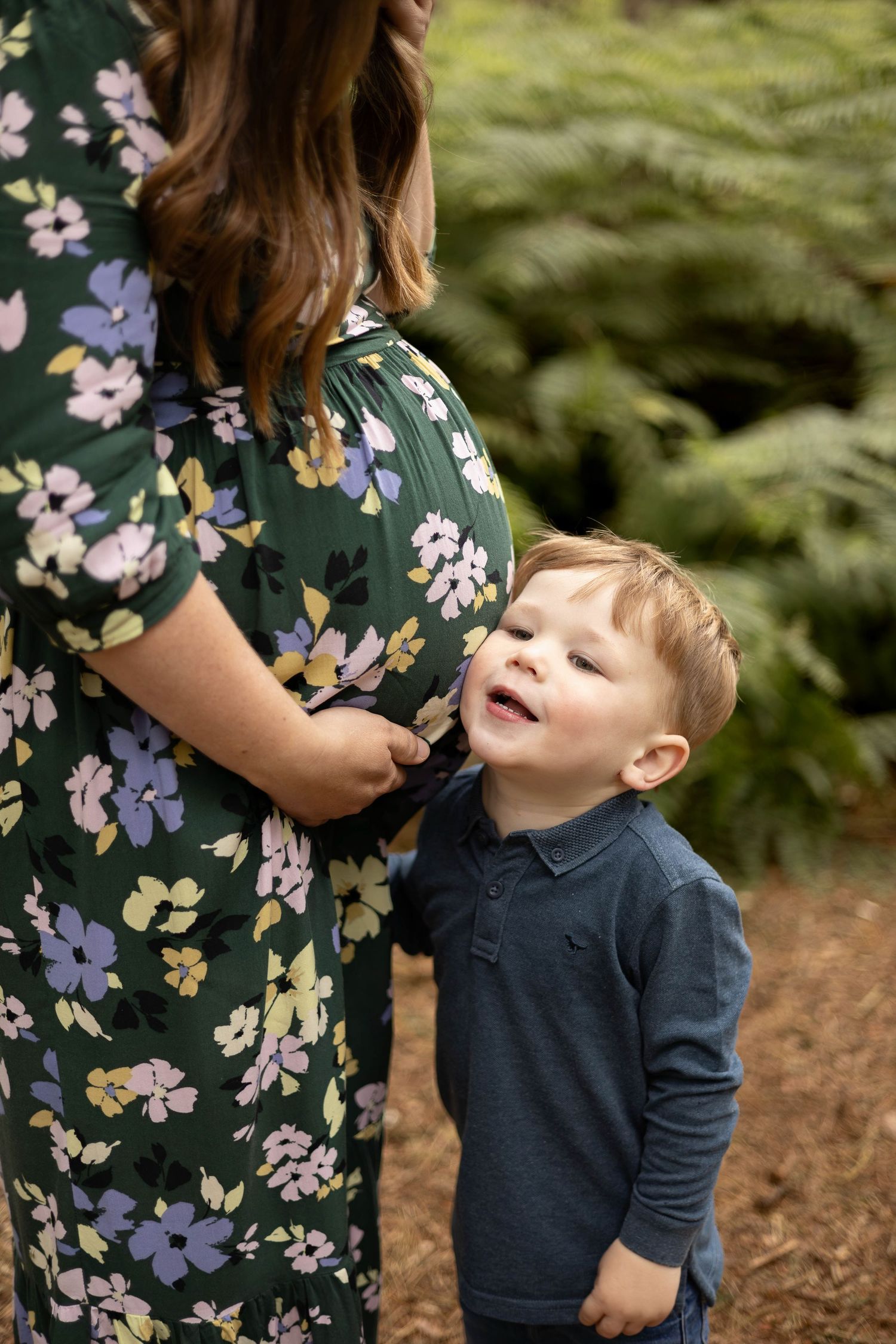 Child in navy shirt smiling next to floral dress in outdoor garden setting.