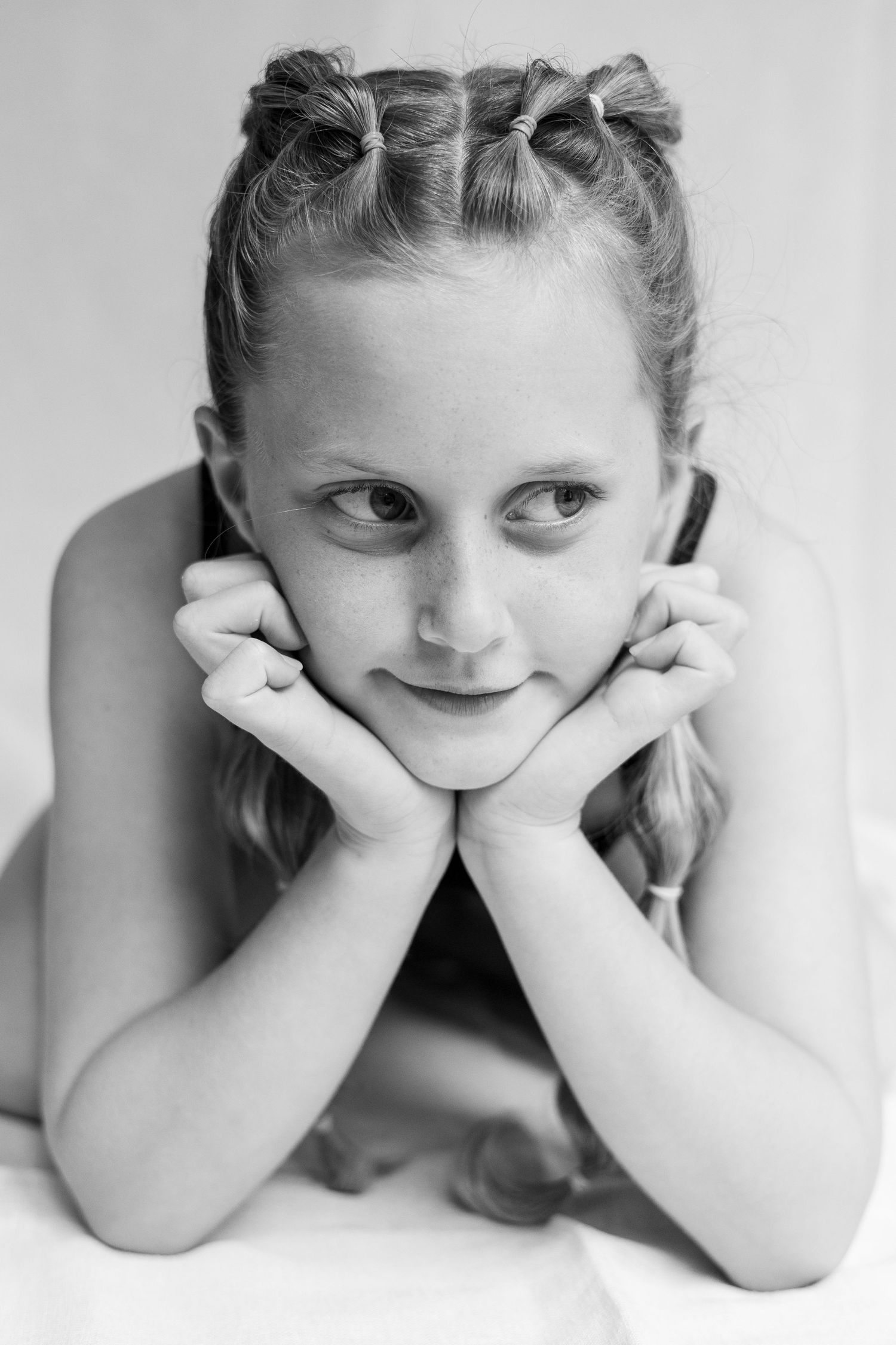 Black and white portrait of a child with pigtails resting their chin on their hands while lying down.