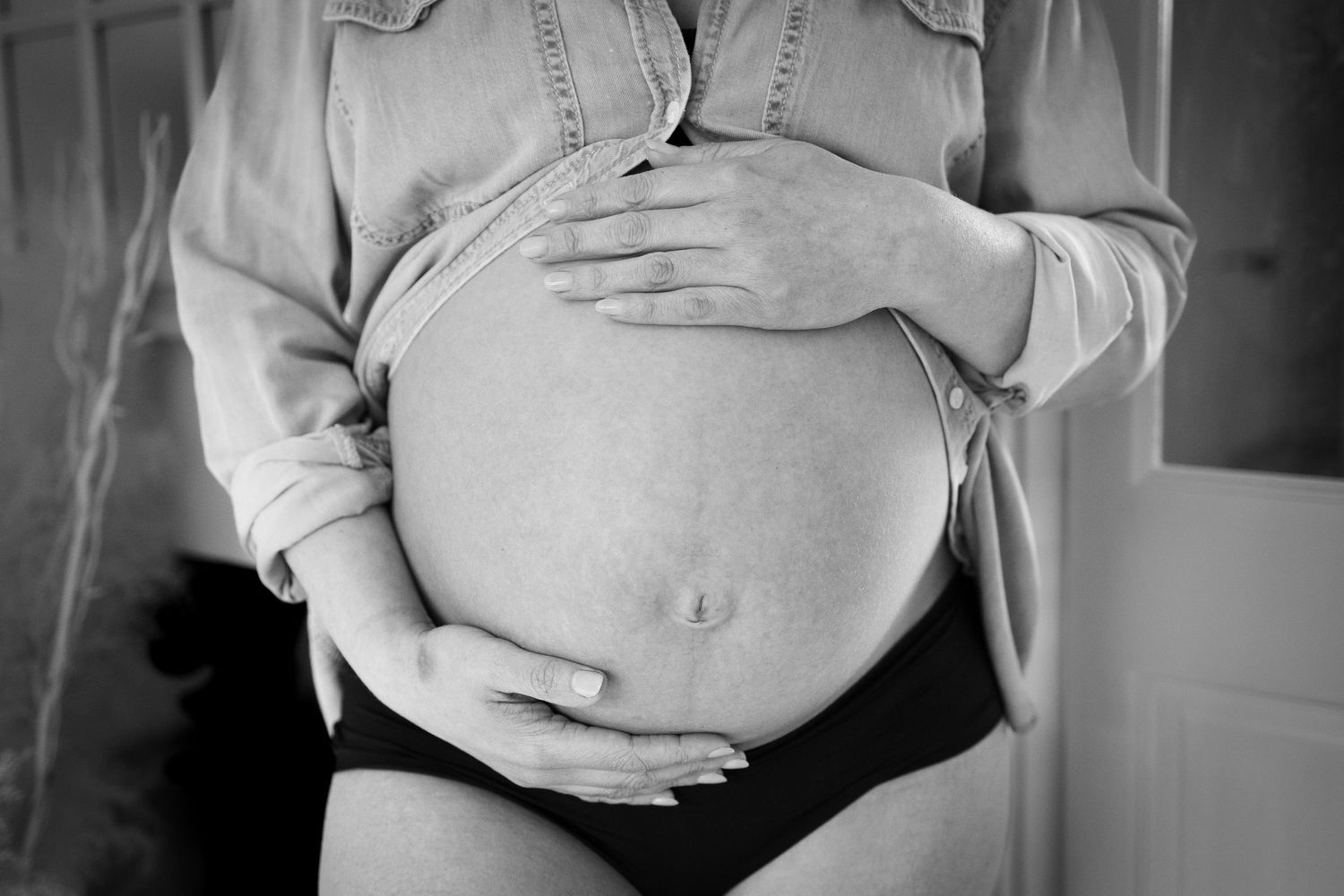 Black and white close-up of hands cradling a pregnant belly while wearing denim.