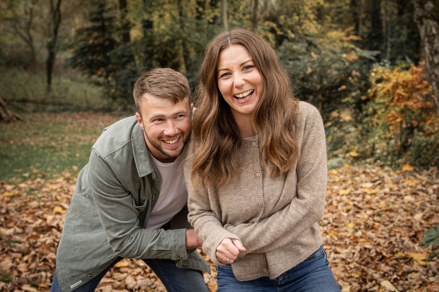 Couple sharing joyful laughter while sitting among fallen autumn leaves in park.