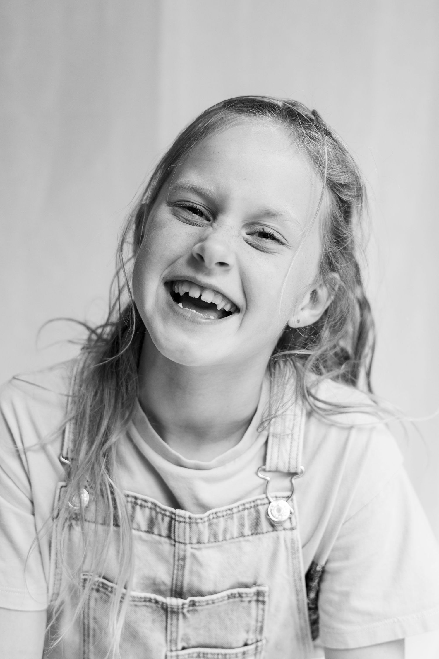 A black and white portrait of a child wearing overalls and laughing with a bright, joyful expression.