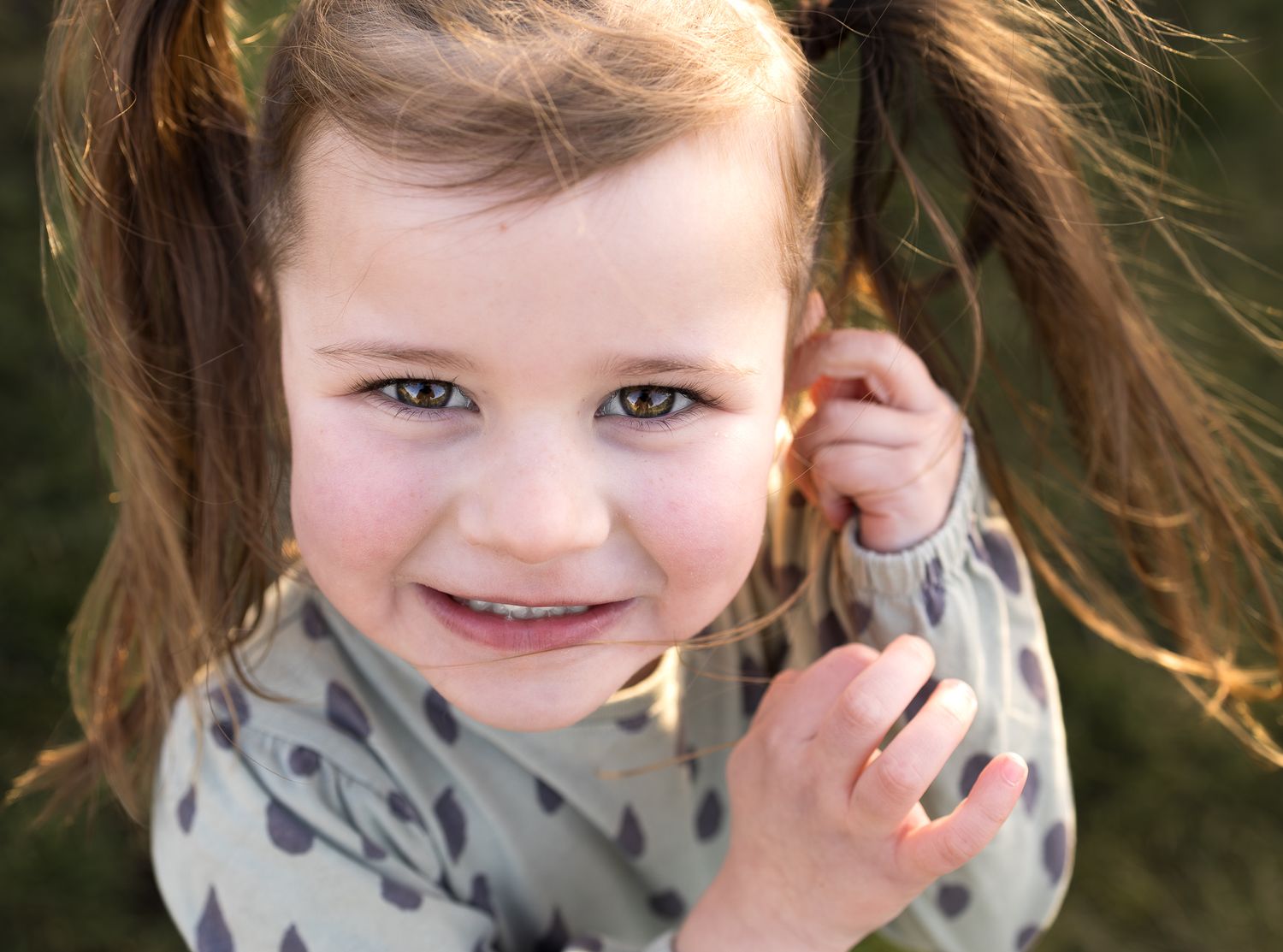 A joyful expression on a young child with pigtails in soft natural light.