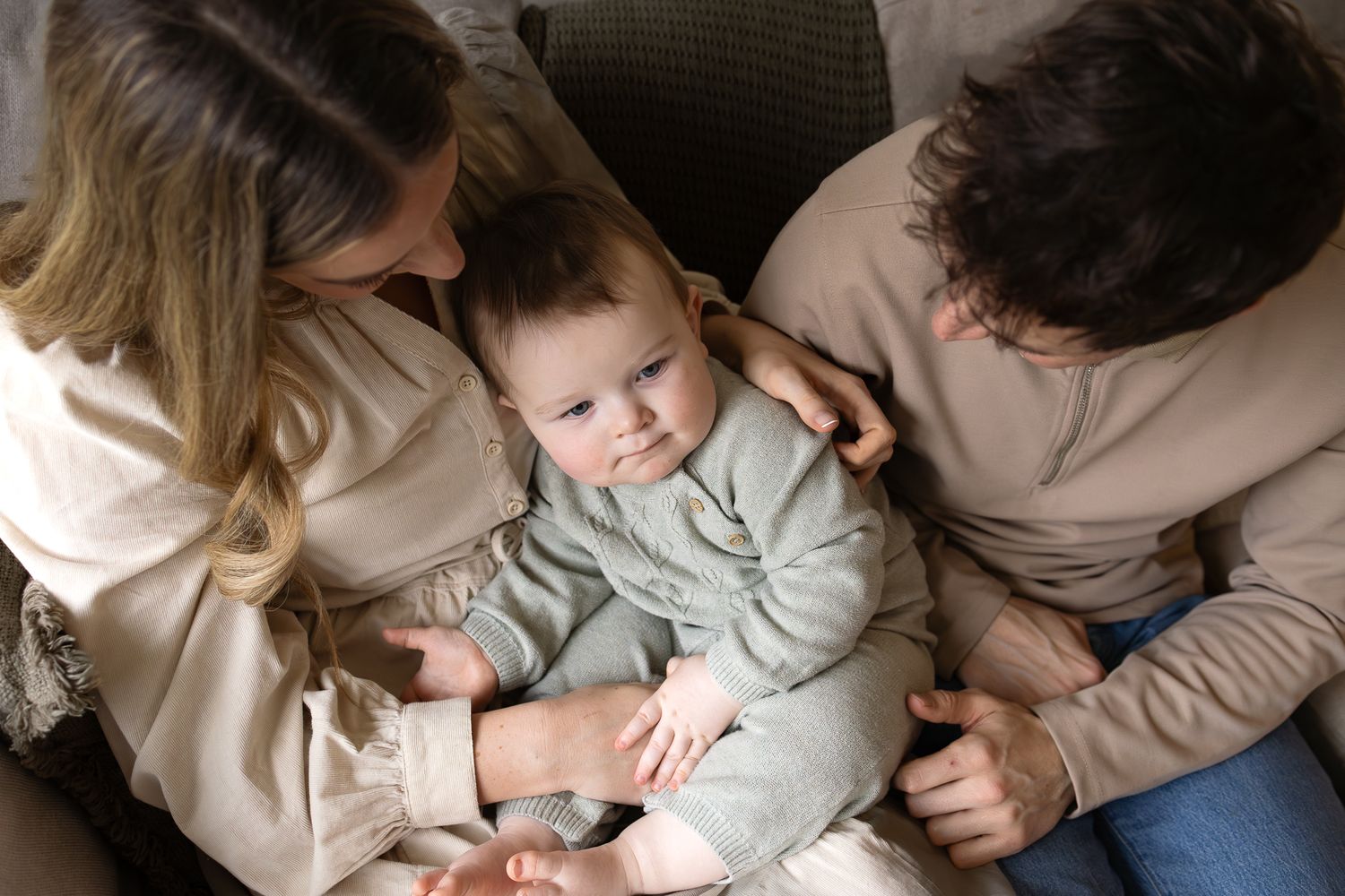 At home family photoshoot in Stamford Bridge, mum, dad and baby share a cuddle on the sofa.