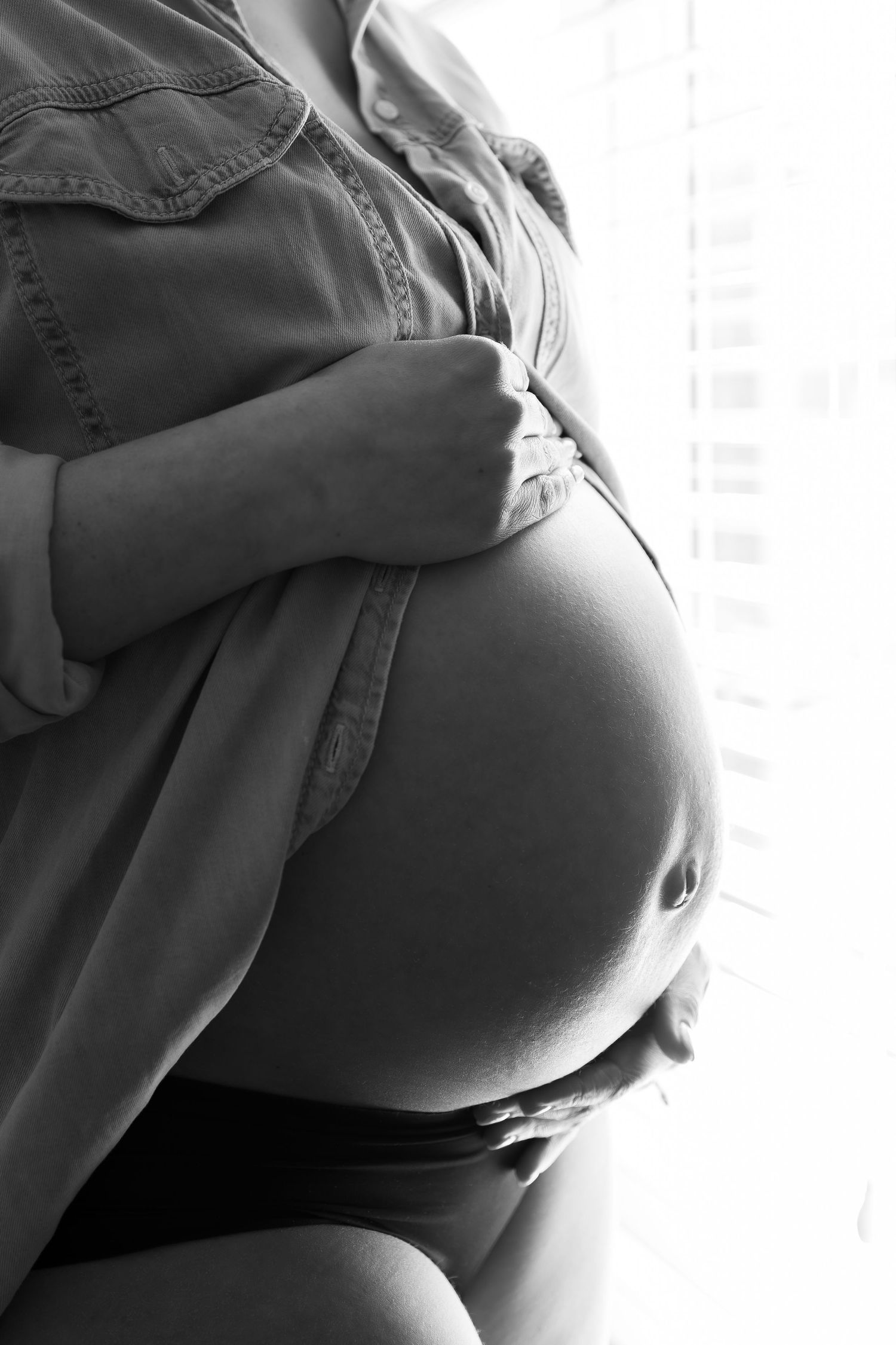 Black and white artistic maternity photograph with dramatic side lighting.