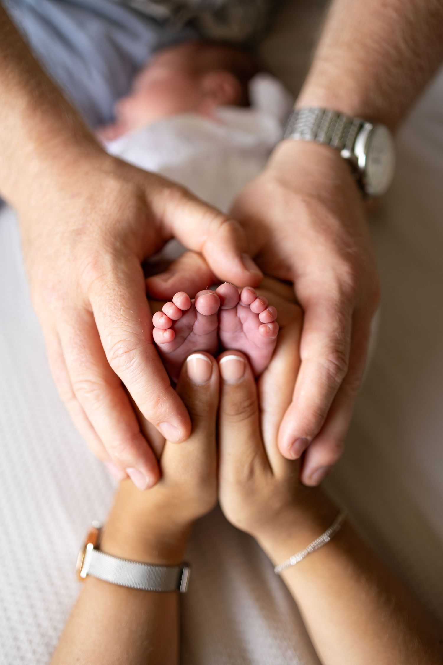 Close-up of tiny baby feet held gently between parent and child hands wearing watches.