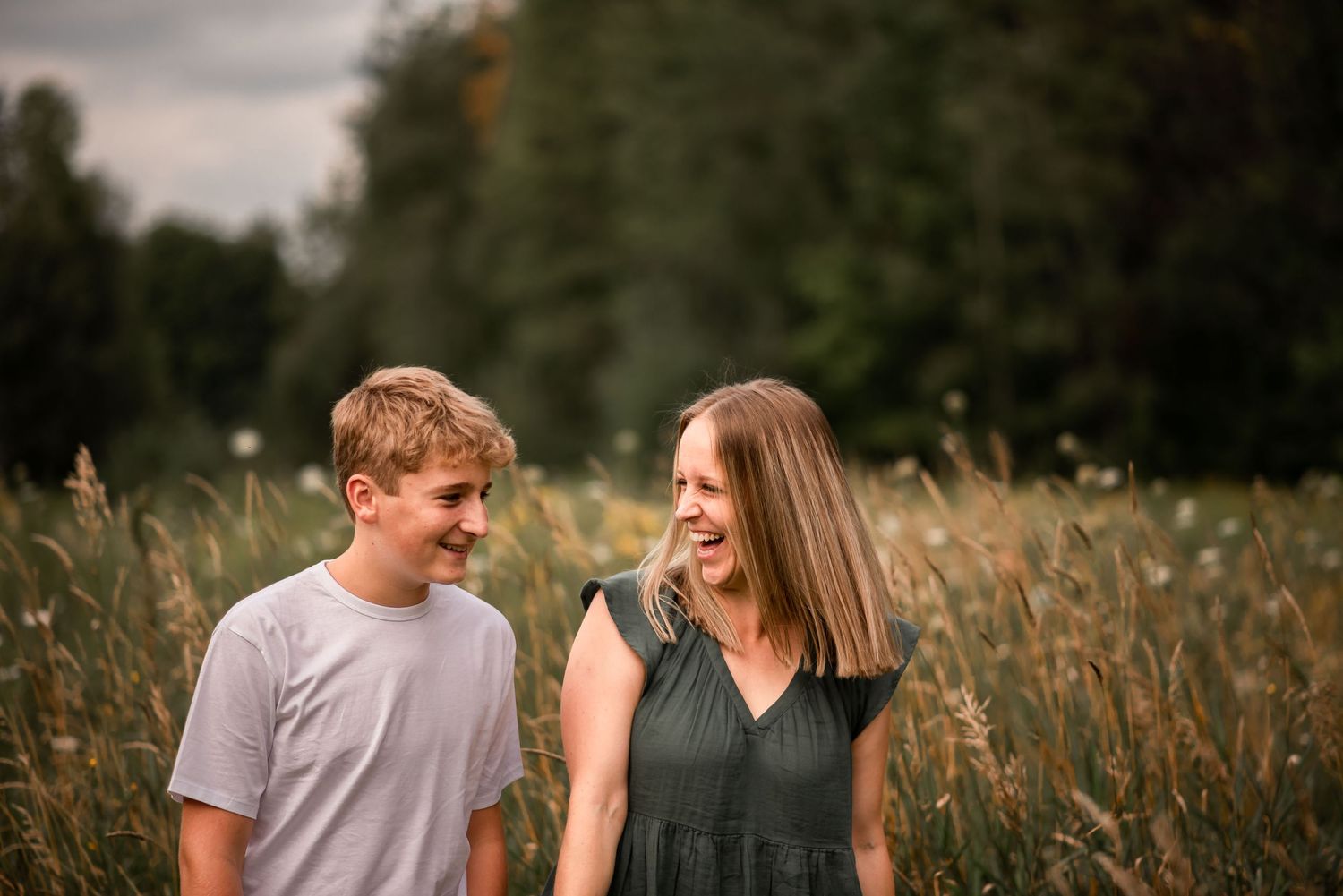 Two people share a joyful moment while standing in a tall grass field at sunset.