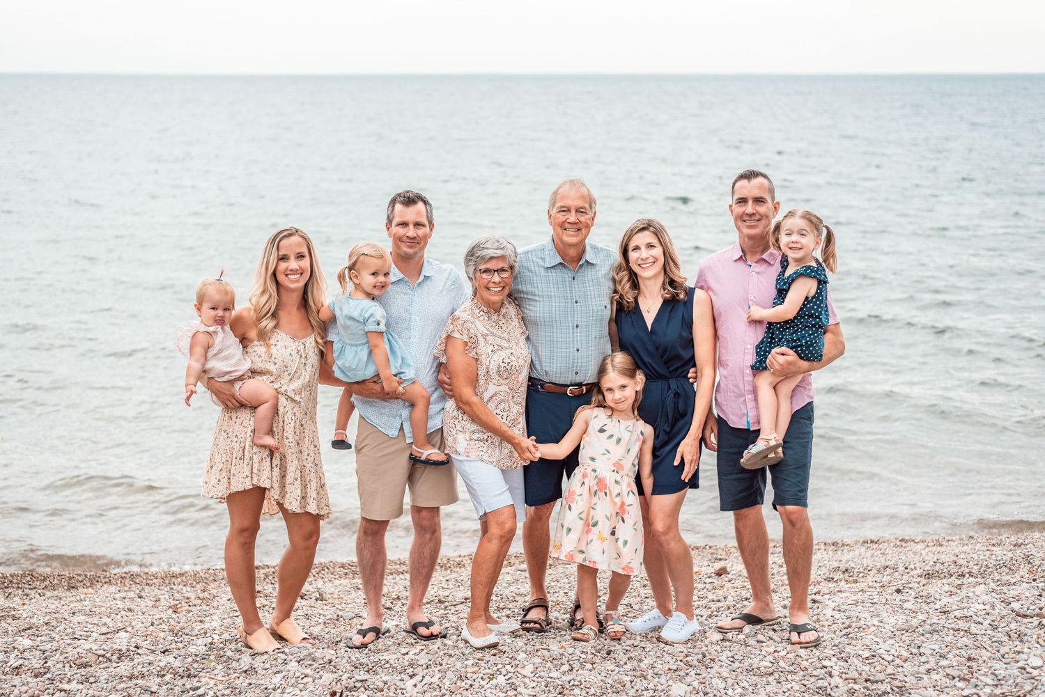 Multi-generational family poses together on beach shoreline in coordinated outfits.