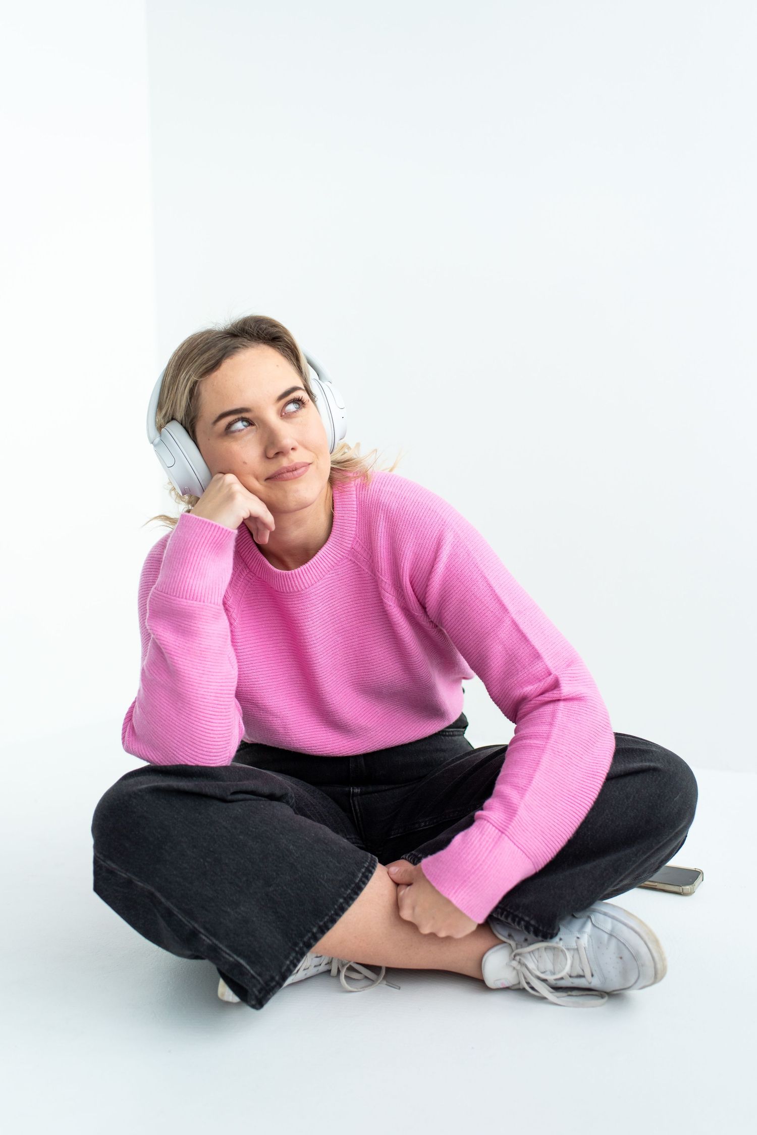 Someone wearing a cozy pink sweater and blue earmuffs sits cross-legged on the floor in a contemplative pose.