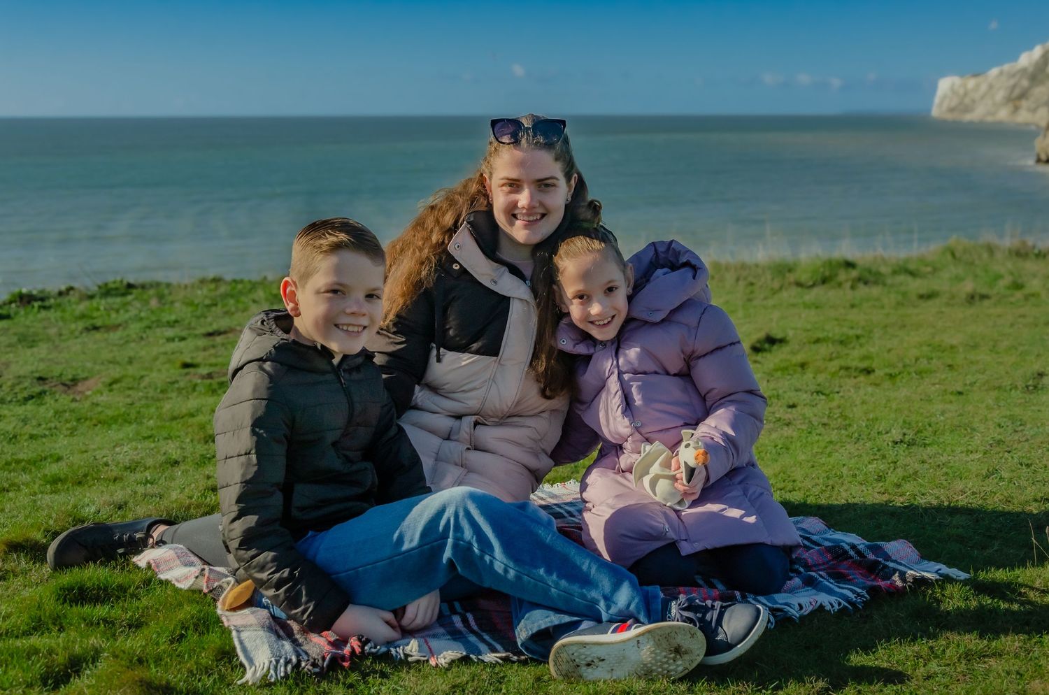 young woman and two young children sat on picnic blanket smiling