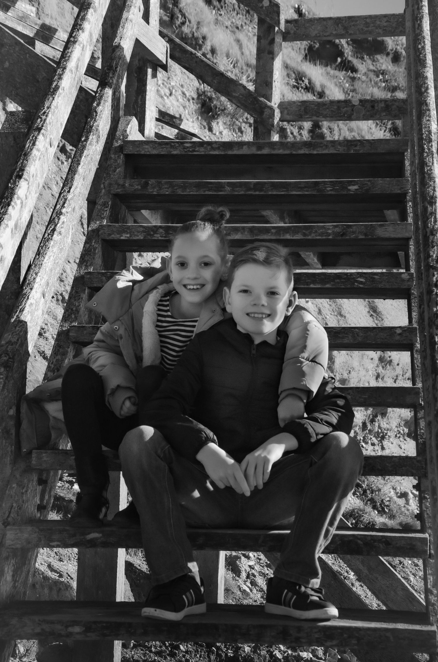 black and white portrait of brother and sister hugging sitting on beach steps