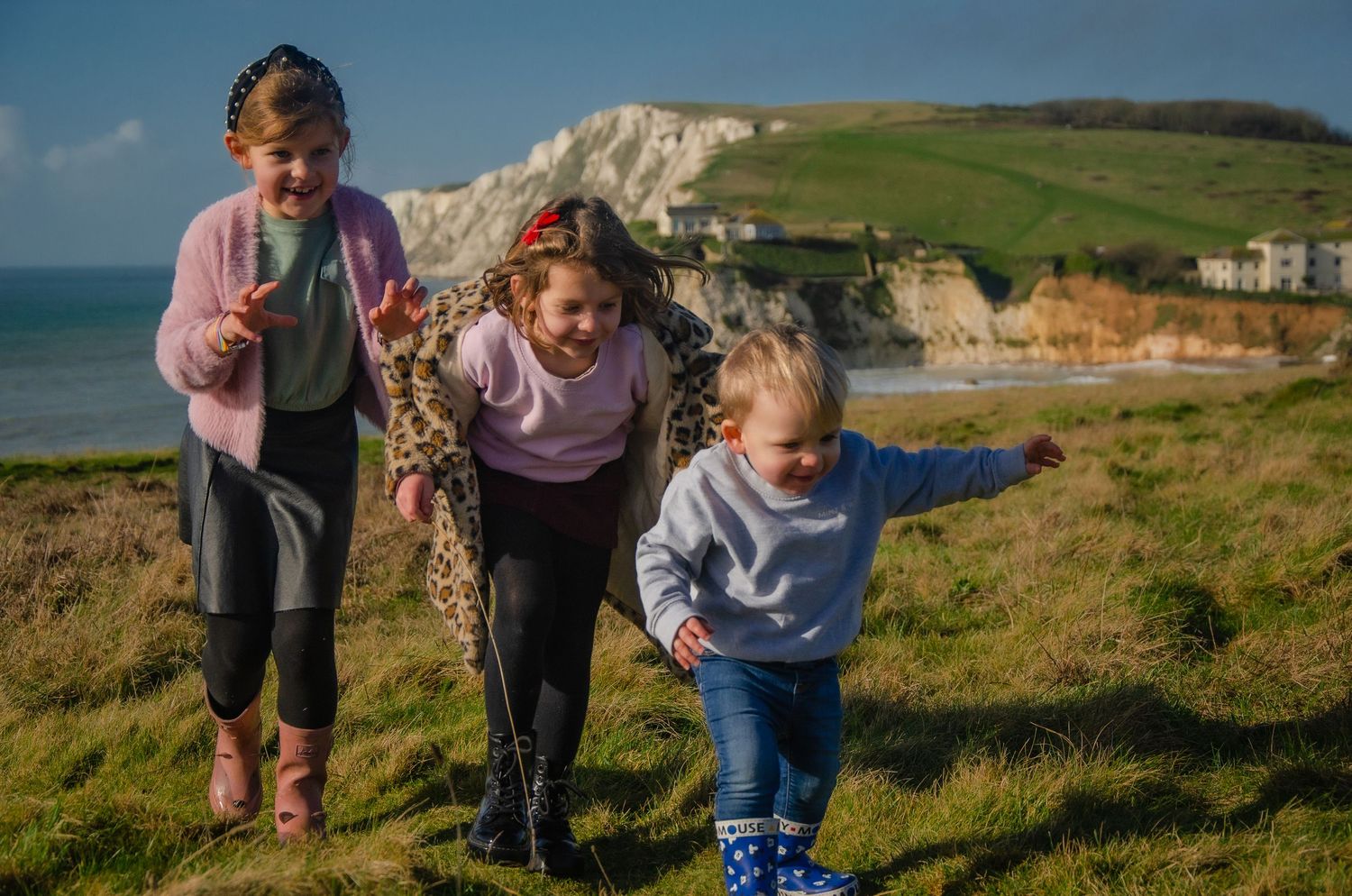three young children chasing each other on grass cliff