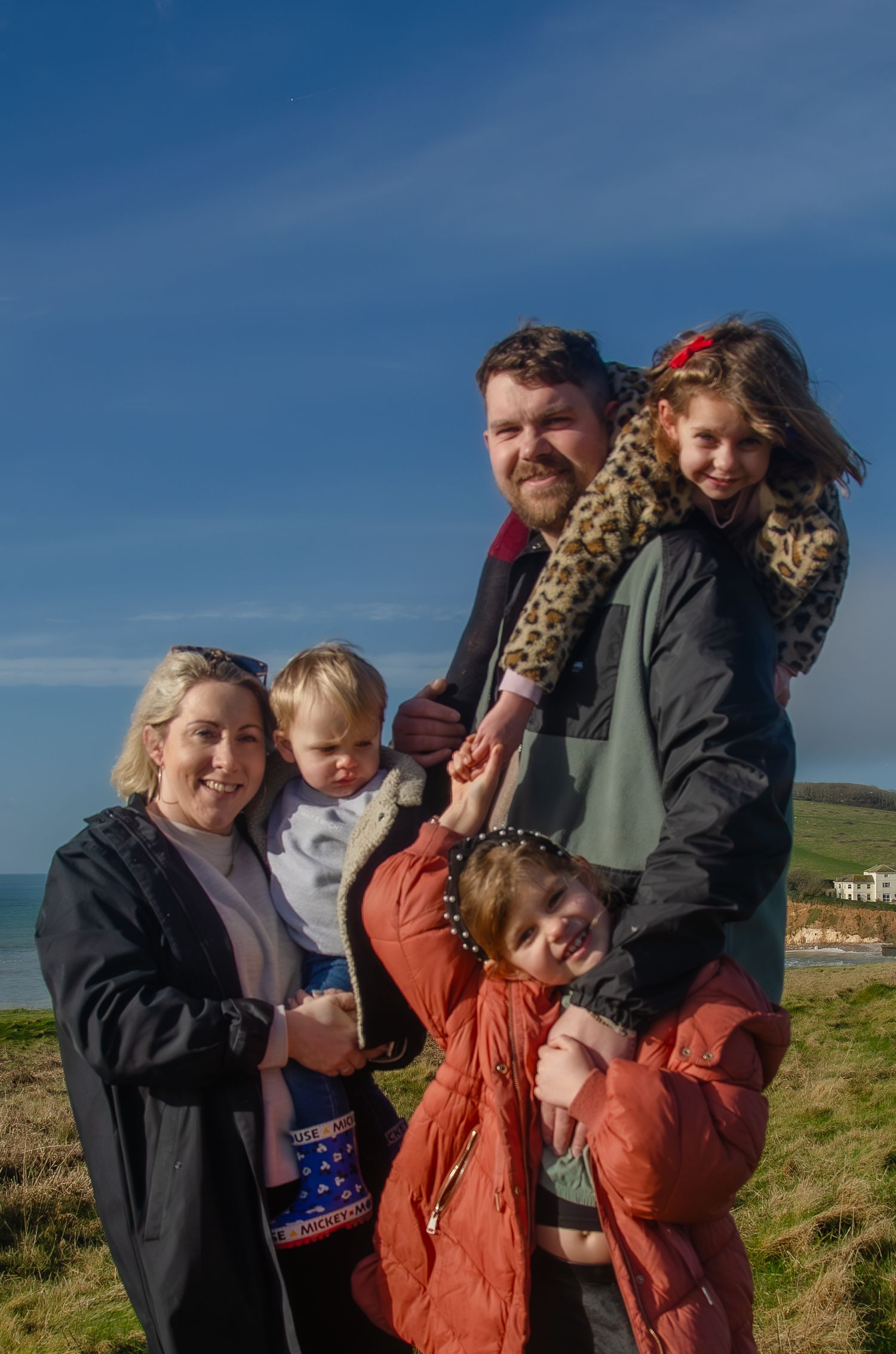family with three young children standing close and smiling