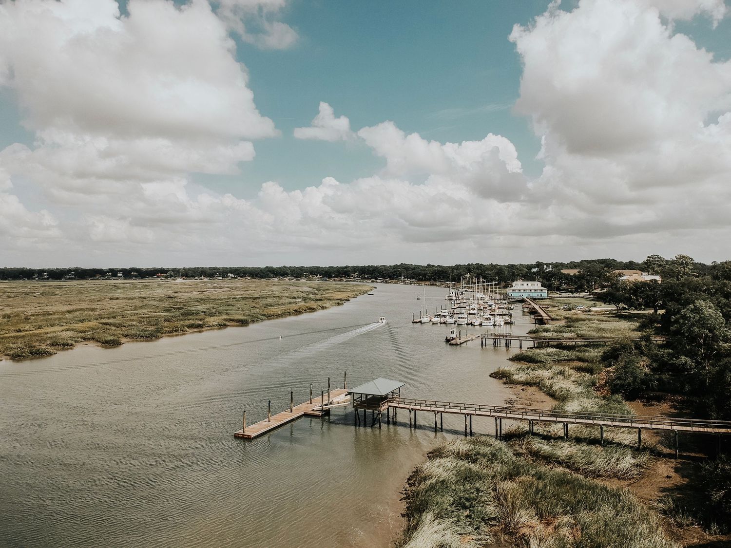 Elevated view of boats moored at a marina next to marsh land under cloudy skies.