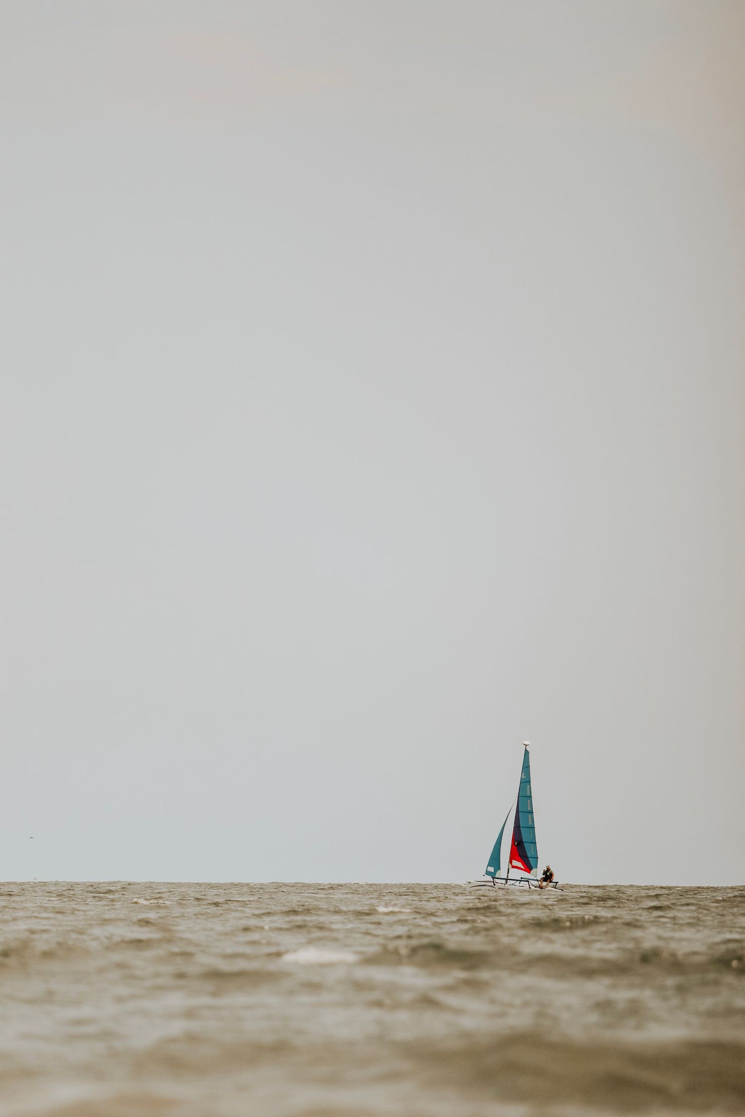 Minimalist shot of single sailboat on choppy waters against misty horizon.
