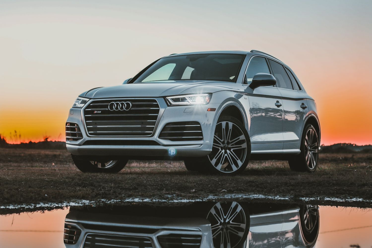 White Audi SQ5 SUV reflects in water during a vibrant sunset.