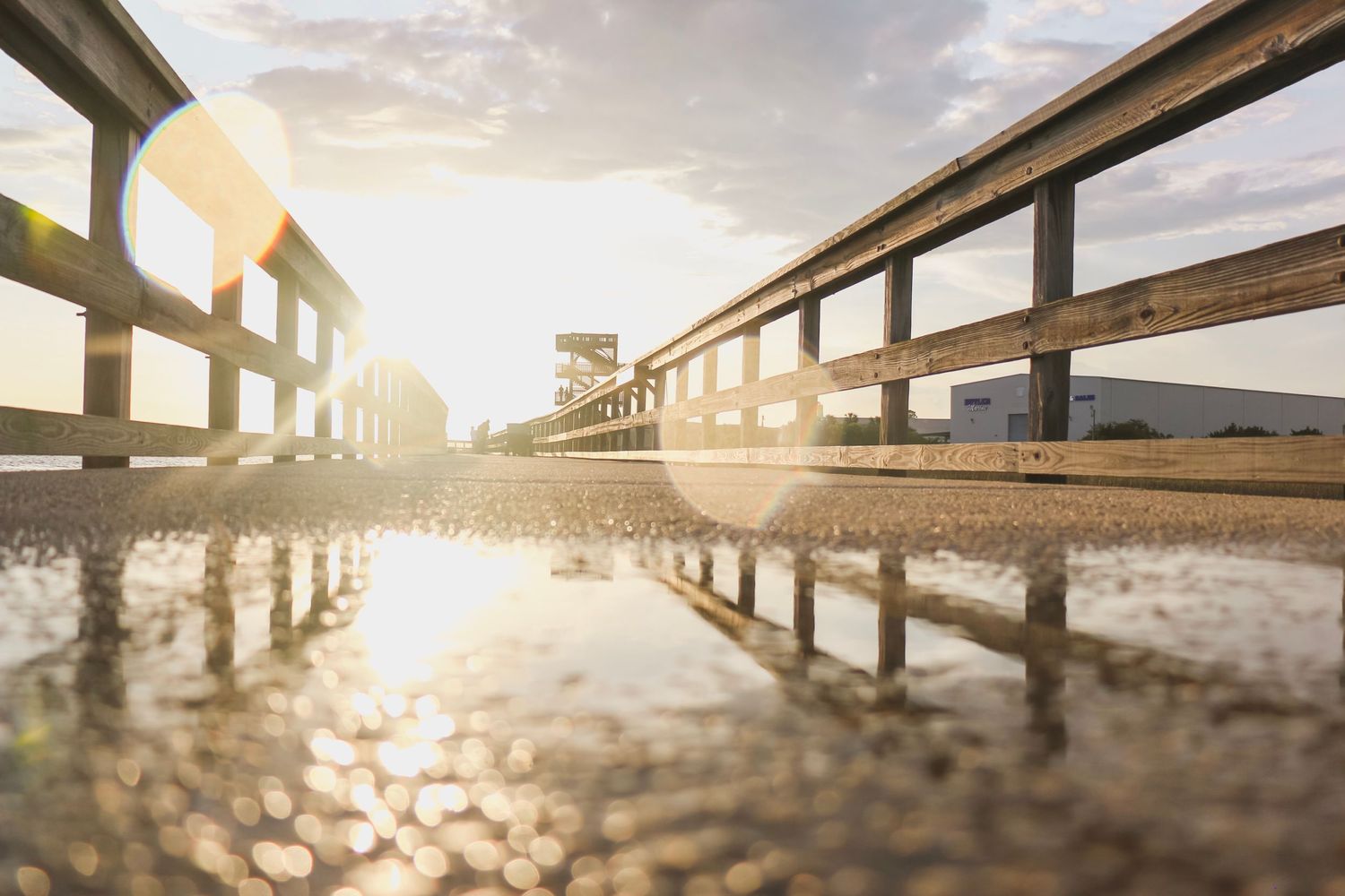 Wooden boardwalk reflected in water during golden sunset.