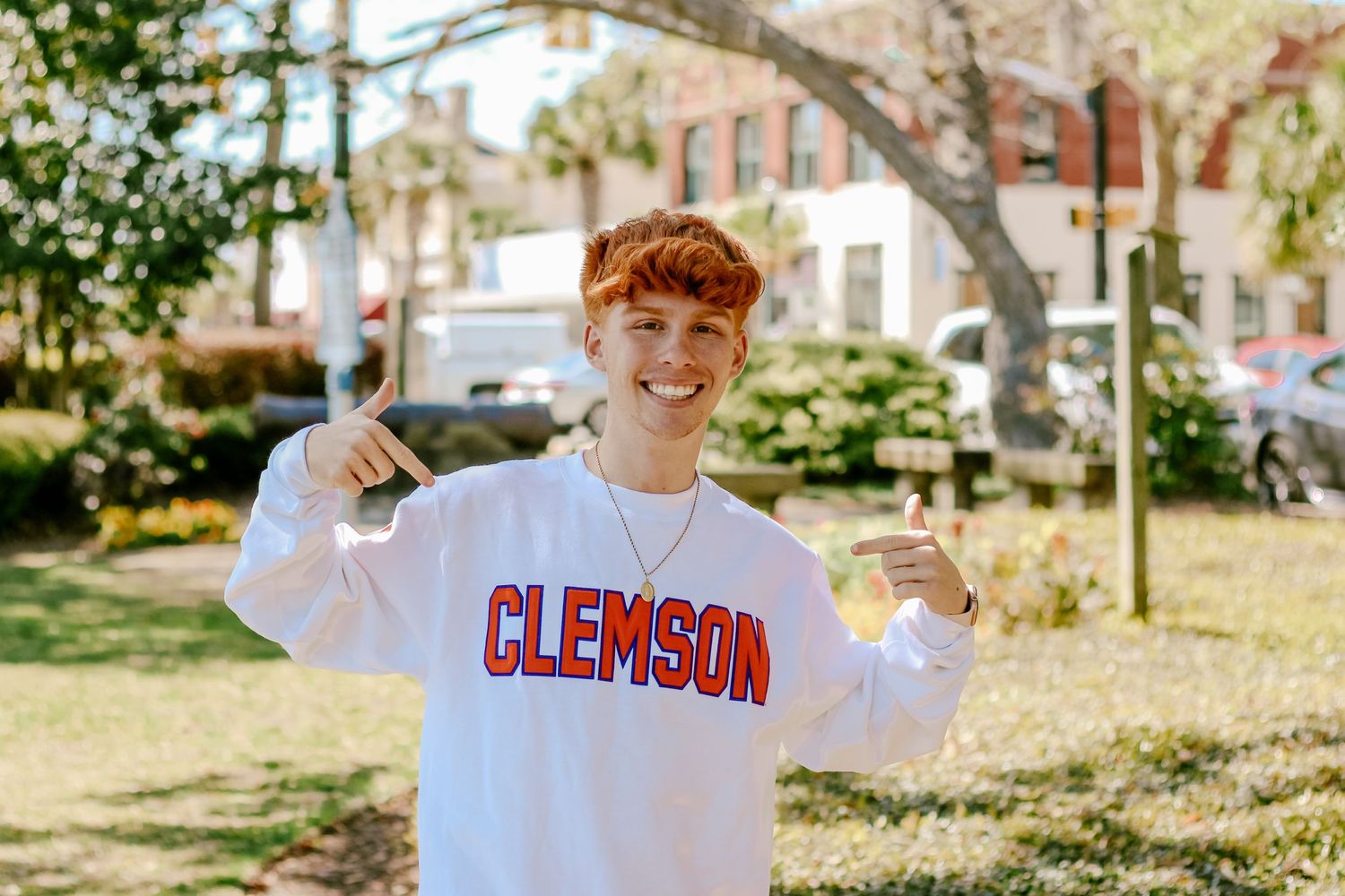 Senior student showing enthusiasm while wearing Clemson University sweatshirt outdoors on campus.