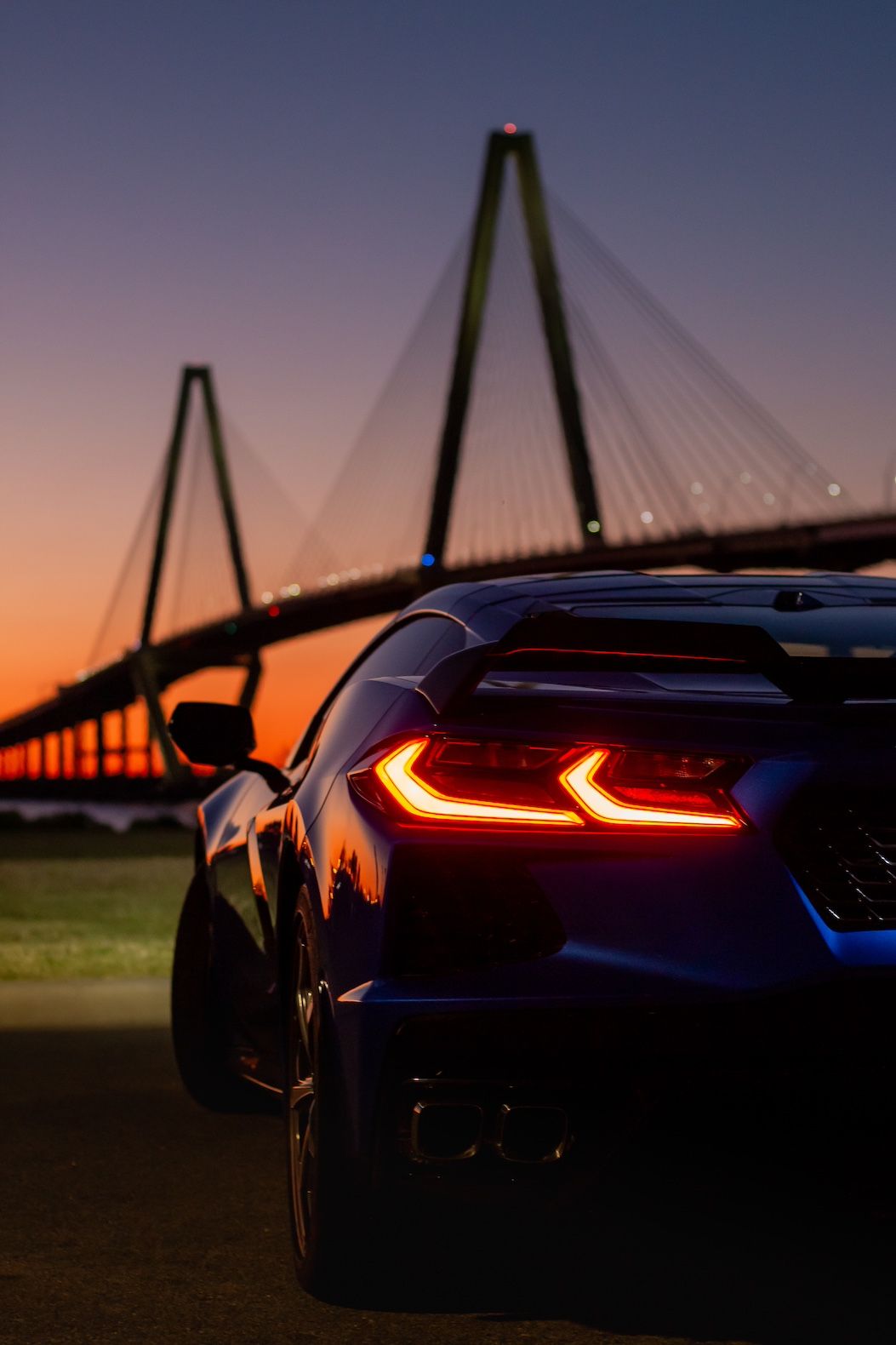 Chevrolet Corvette C8 tail light glows at sunset with Arthur Ravenel Jr Bridge silhouetted in Charleston, South Carolina.
