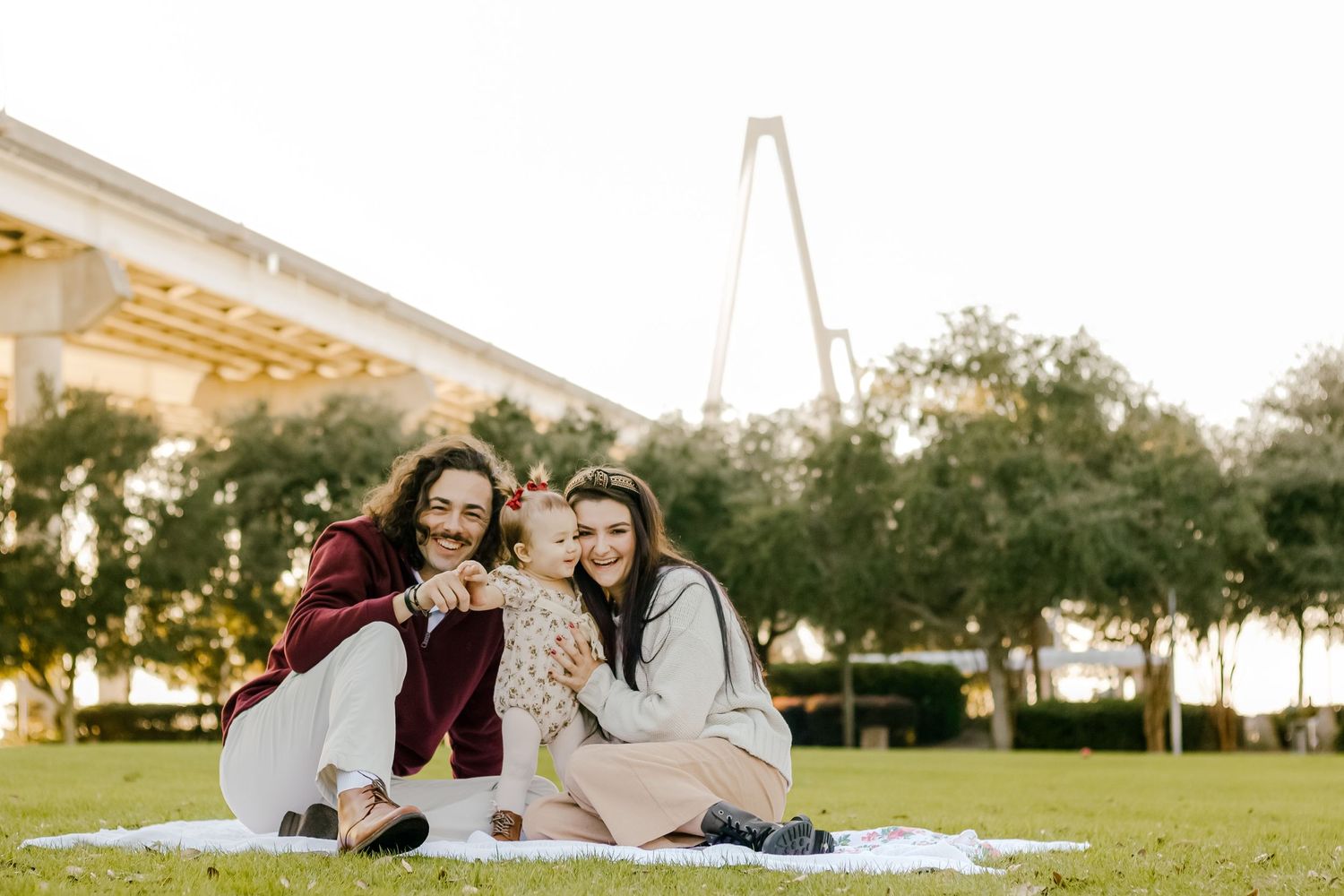 Small family sharing joyful moment during outdoor picnic near Charleston bridge.