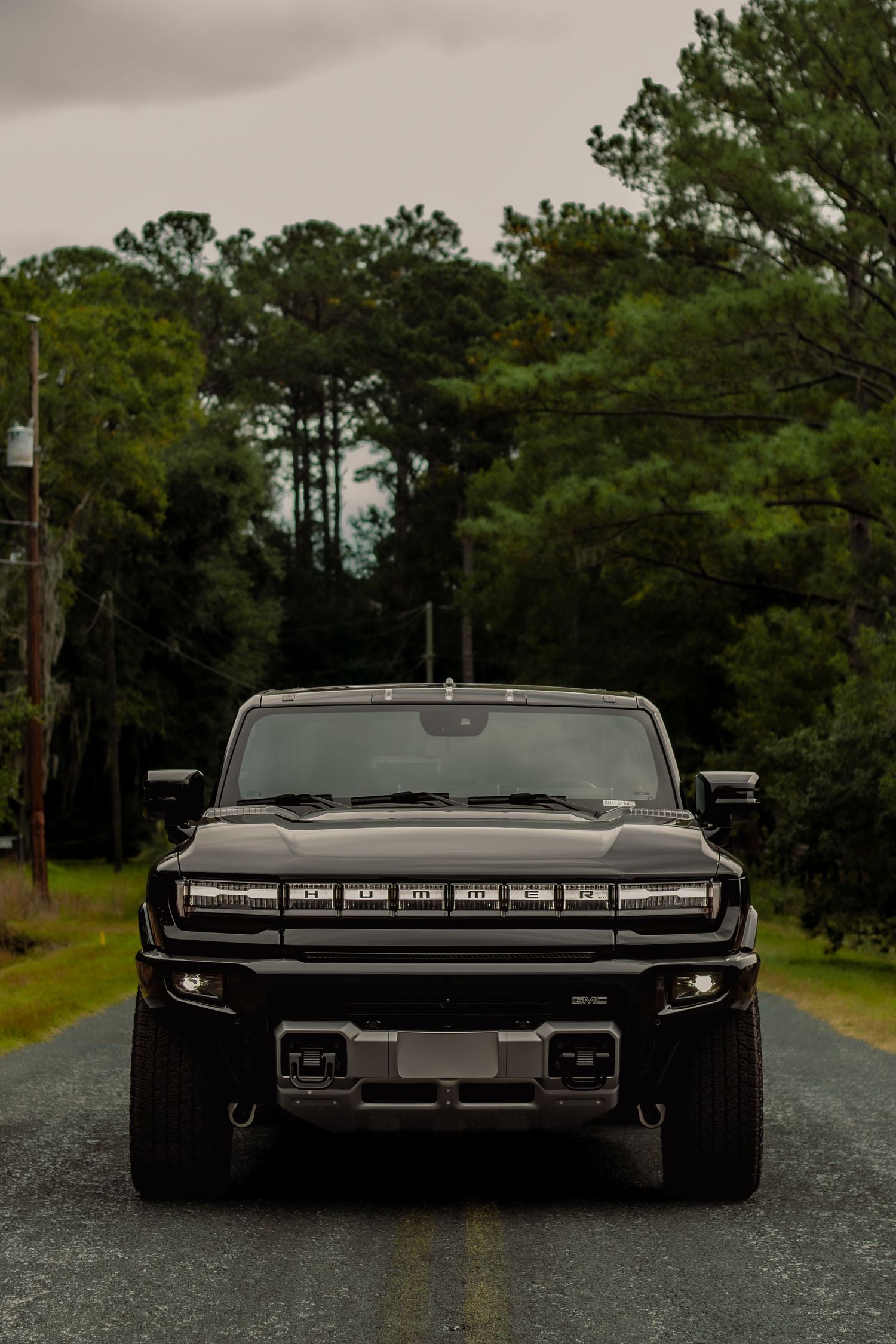 A sleek black vintage car photographed from different rear angles on a tree-lined road in moody lighting.