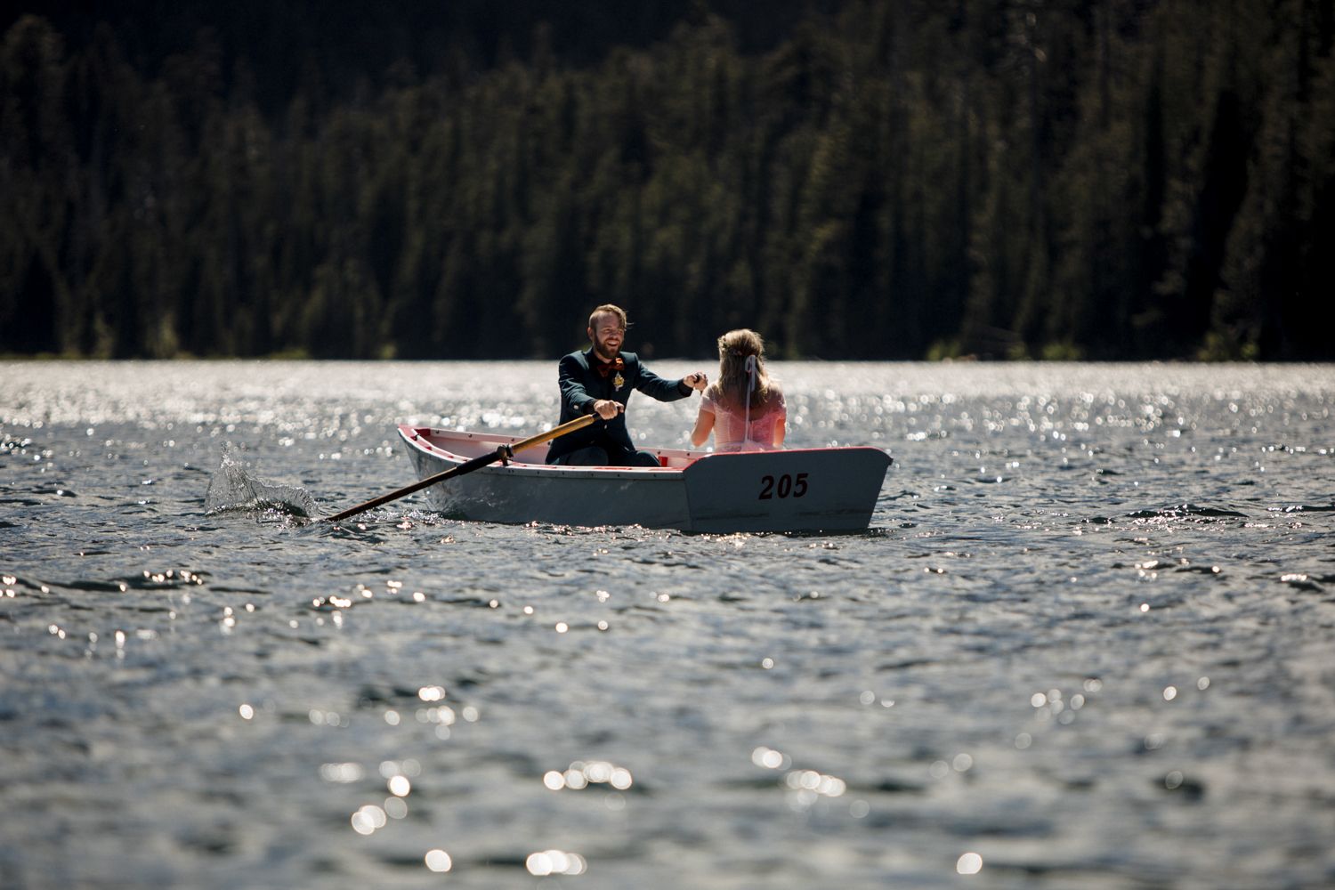 A couple rowing together in a small boat on a sunlit mountain lake.
