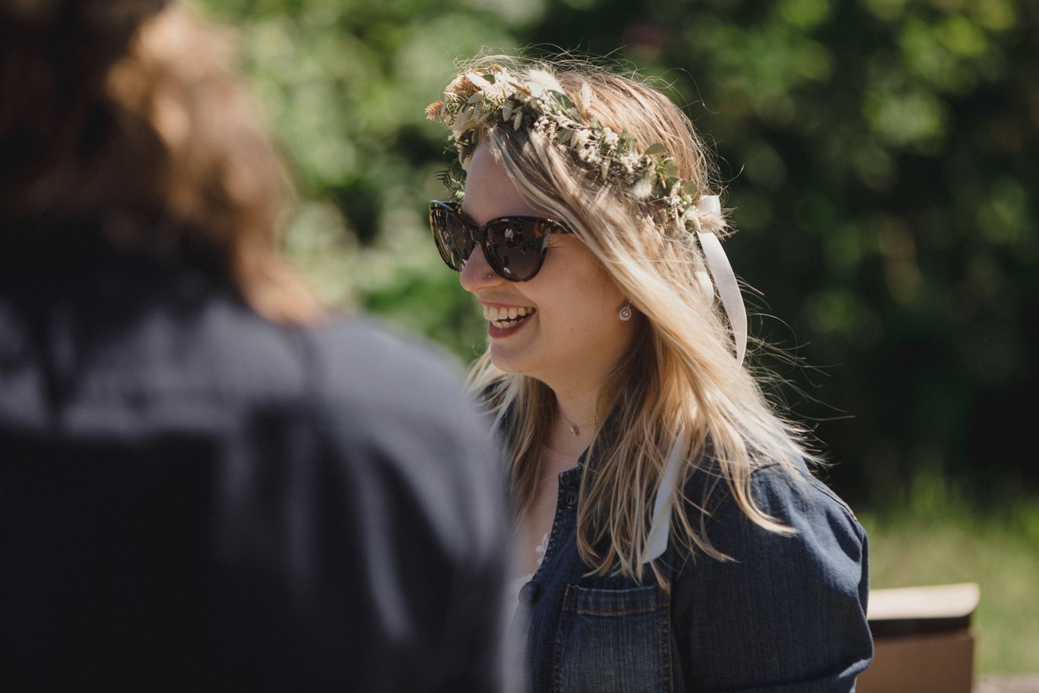 Someone wearing a floral crown and sunglasses smiles outdoors on a sunny day.
