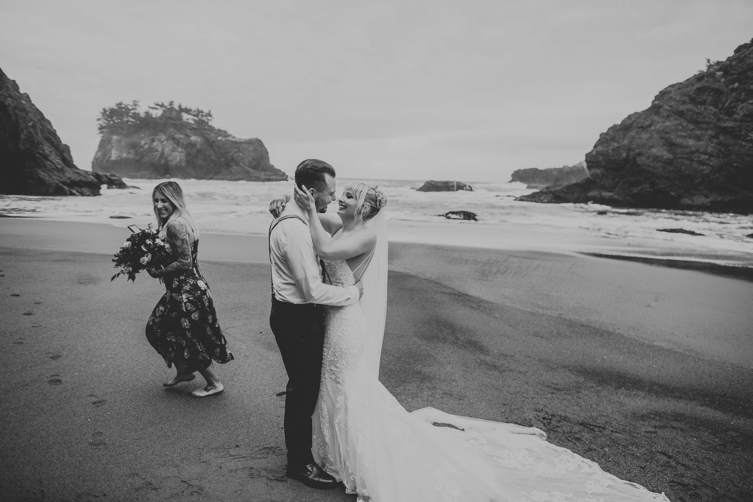 A black and white photo of a wedding ceremony on a secluded beach surrounded by rocky cliffs.