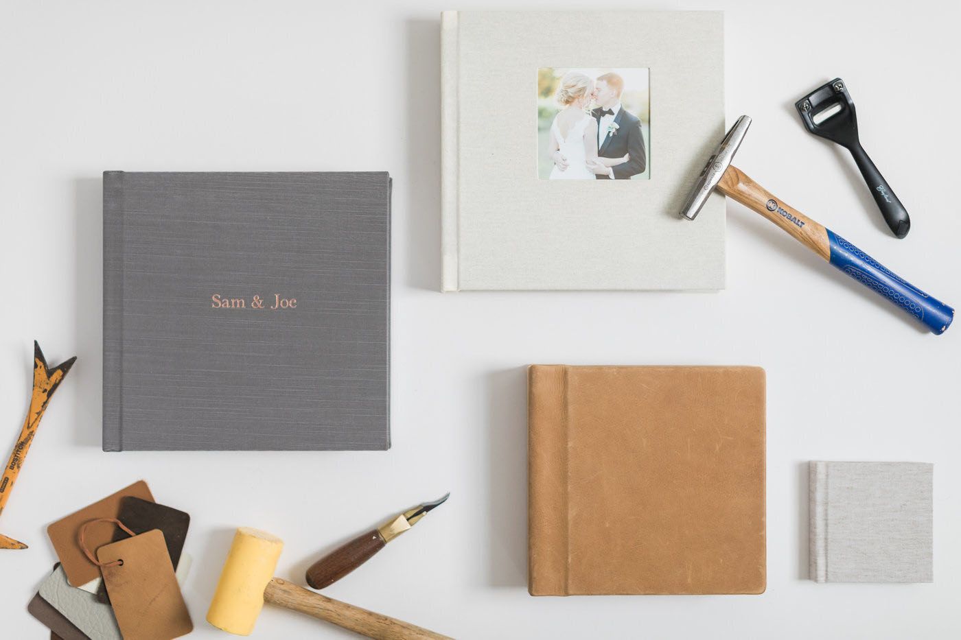 Three handmade photo albums with bookbinding tools, including a brayer and bone folder, on a white surface.