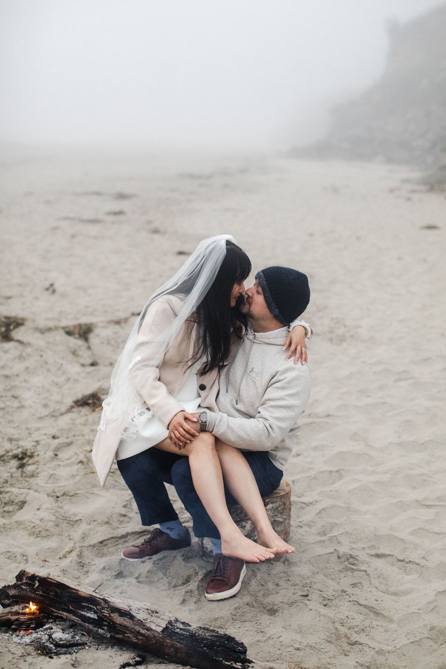 Couple sharing a kiss by a beach bonfire on a misty sandy shore.