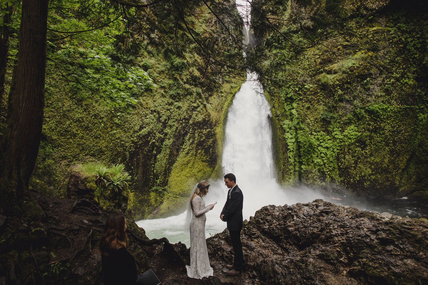 Couple standing together in front of a majestic waterfall with moss-covered cliffs in Oregon's Columbia River Gorge.