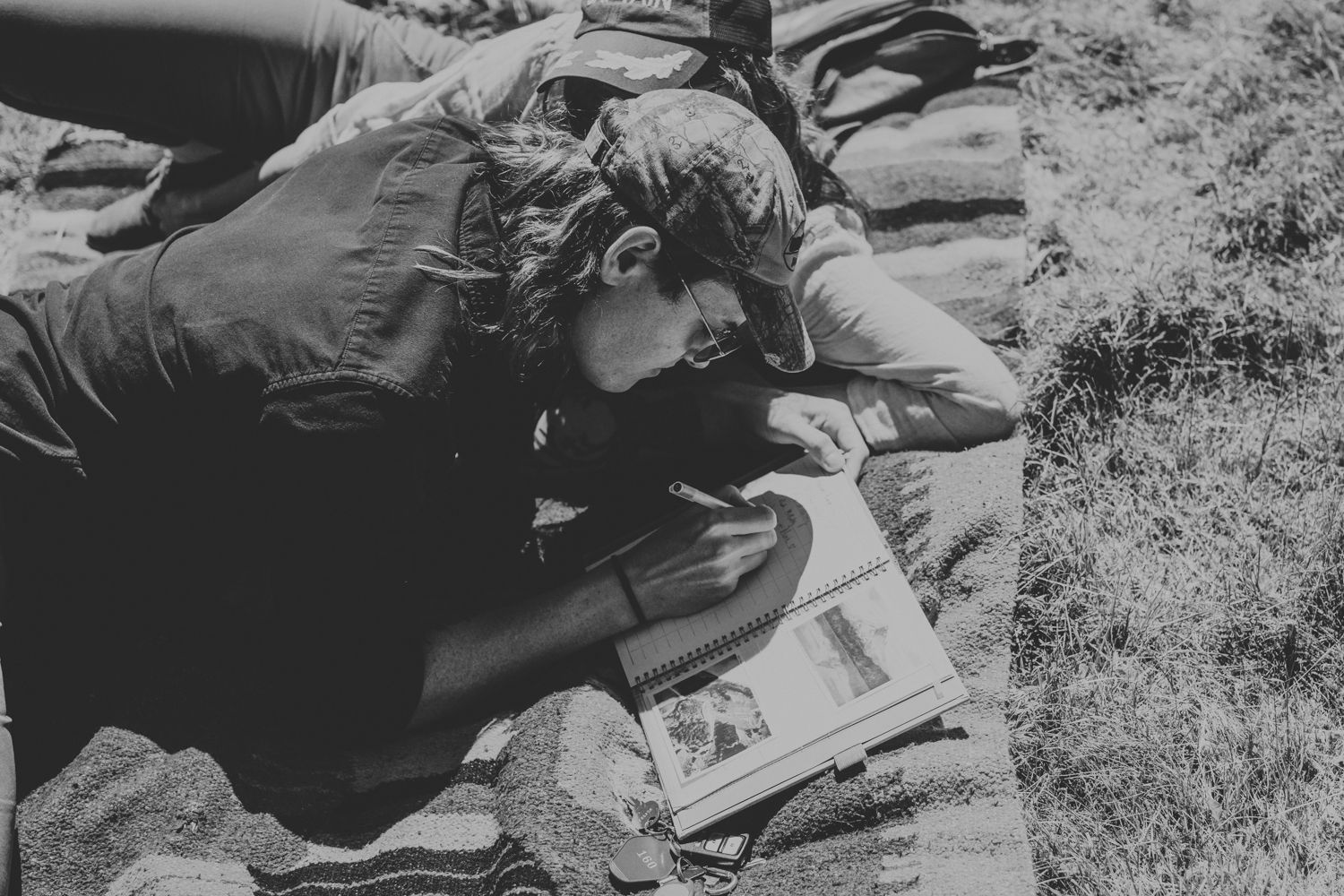 Black and white photo of someone reading or writing in an outdoor setting.