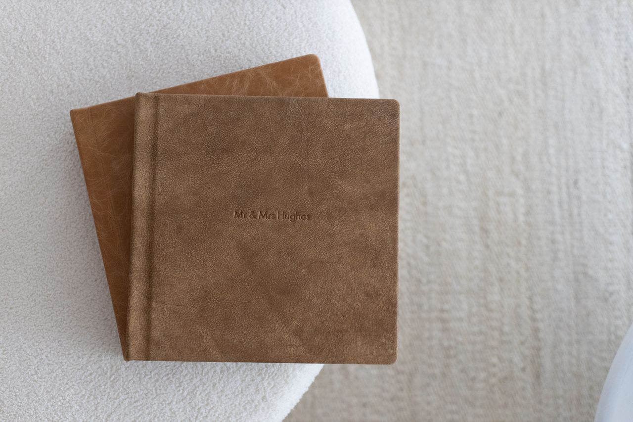 Two brown leather photo albums stacked on a white textured surface with embossed text on the cover.