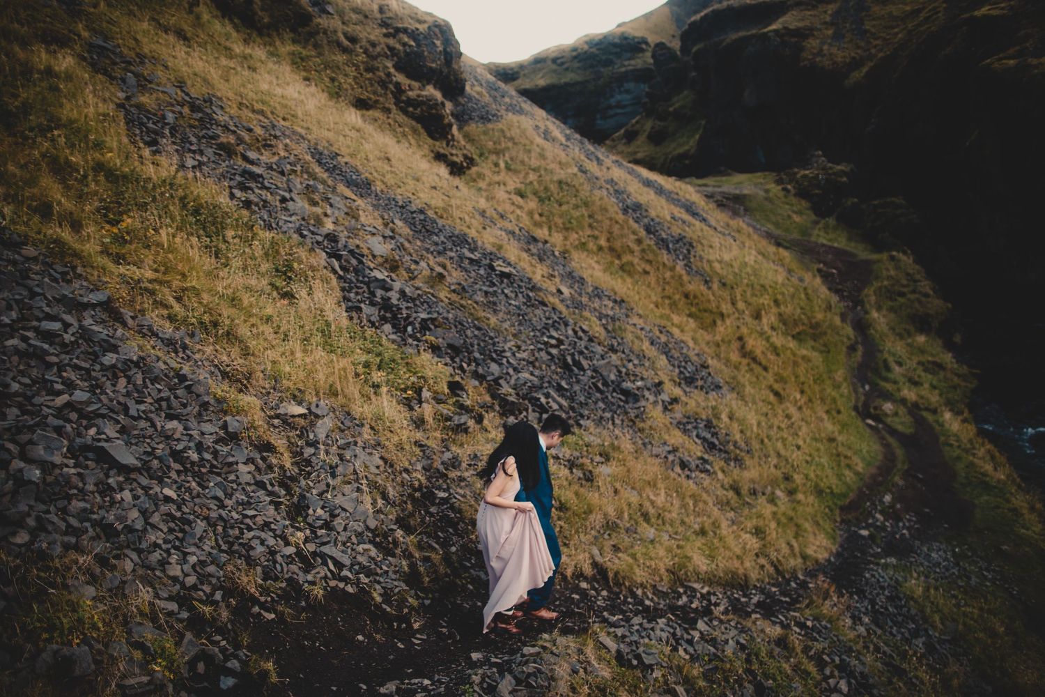 Two people walking up steep mountain path with dramatic valley views.