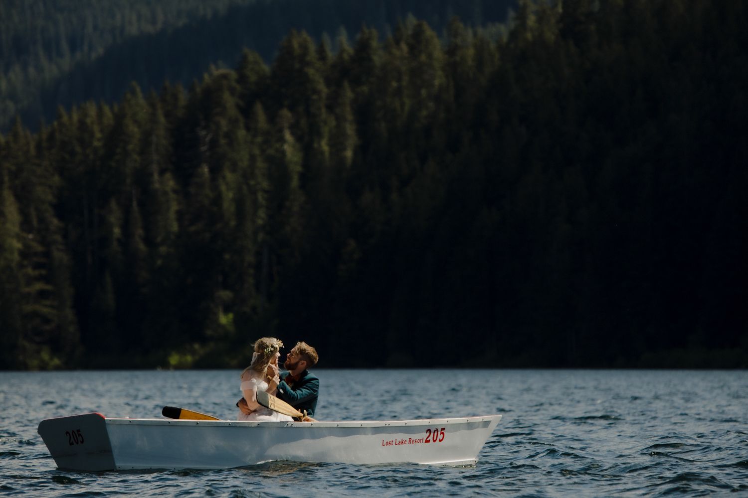A couple sits close together in a small boat on a mountain lake.