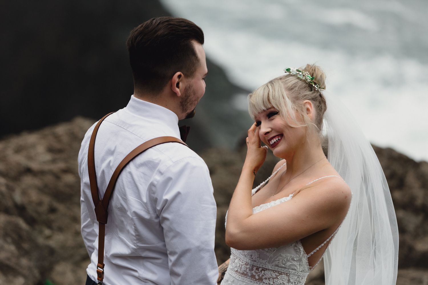 A joyful wedding moment shared between newlyweds on a rocky ocean overlook.