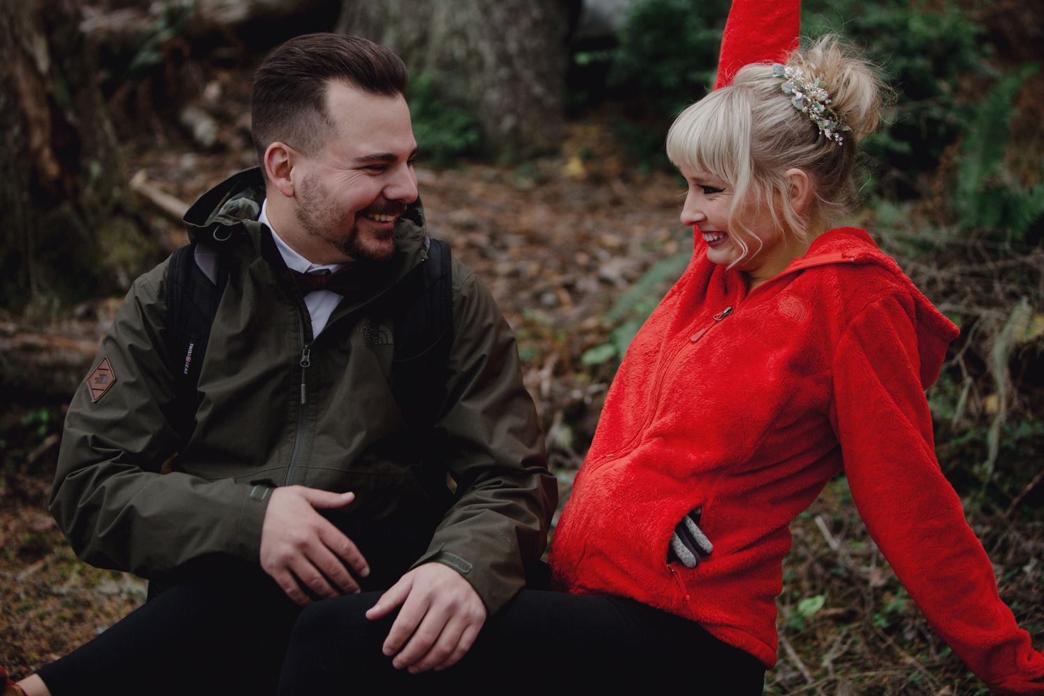 A casual outdoor portrait of a couple laughing together while wearing red and green jackets.