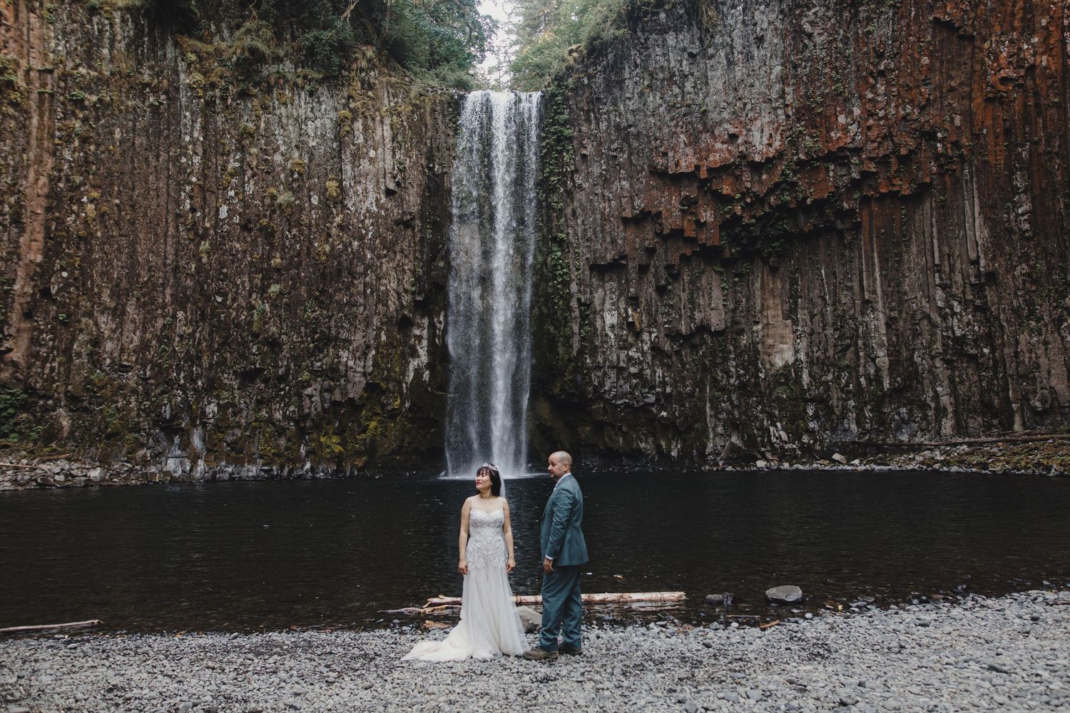 Bride and groom standing before a stunning waterfall with basalt columns during their elopement.