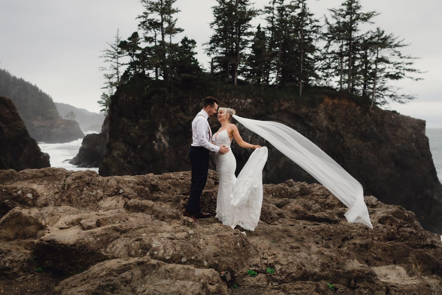 A dramatic wedding portrait with flowing veil against rugged coastal cliffs and ocean views.