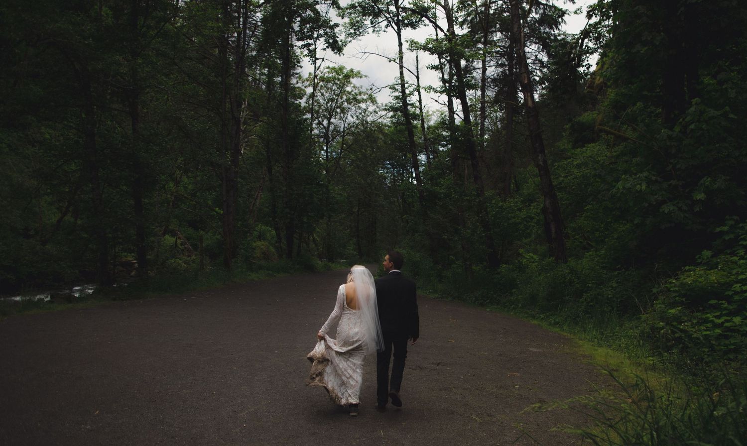 A wedding couple walking together on a winding forest path.