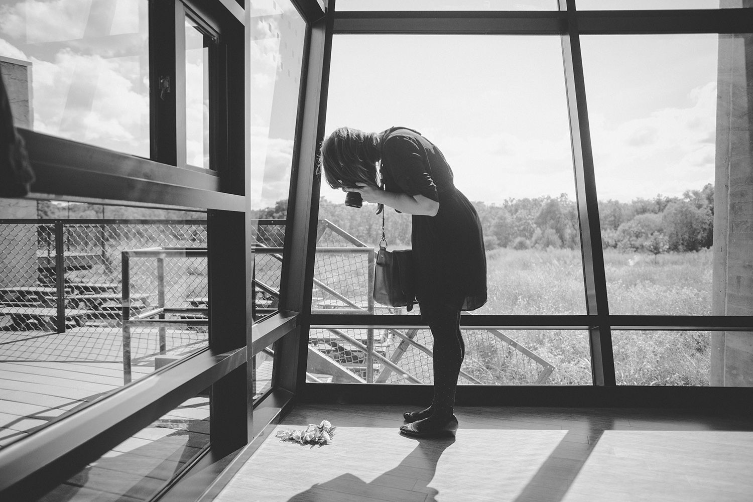 Black and white photo of a person bending over near large windows overlooking a field in a modern building.