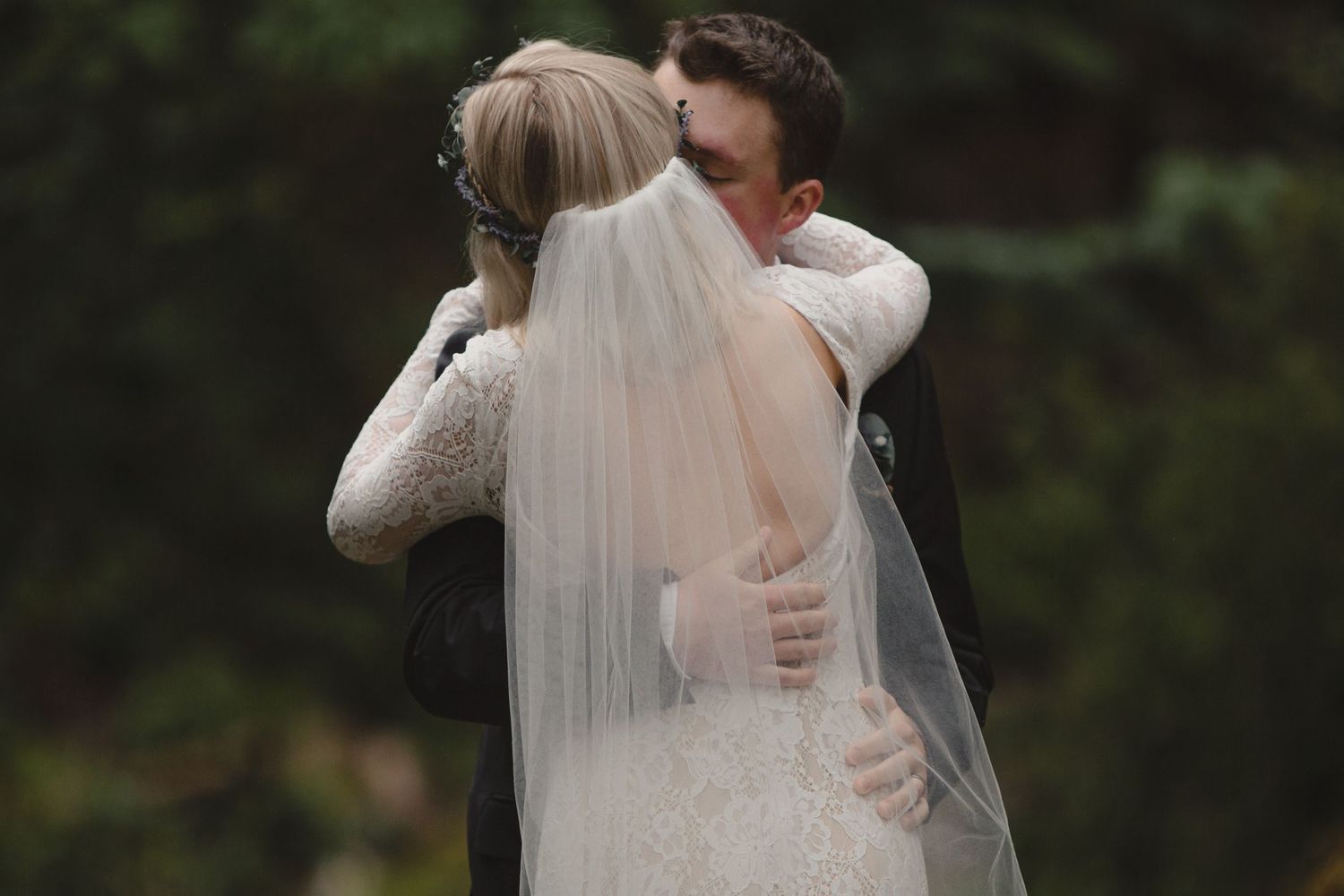 A tender embrace between newlyweds with a flowing white veil in natural lighting.