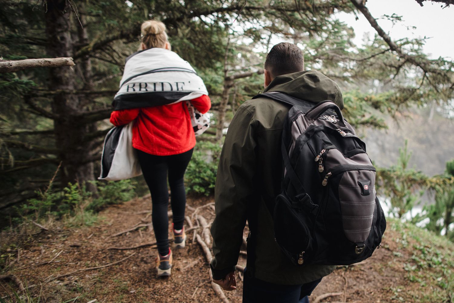 Hikers traverse a scenic forest trail along the coastline with backpacks and outdoor gear.