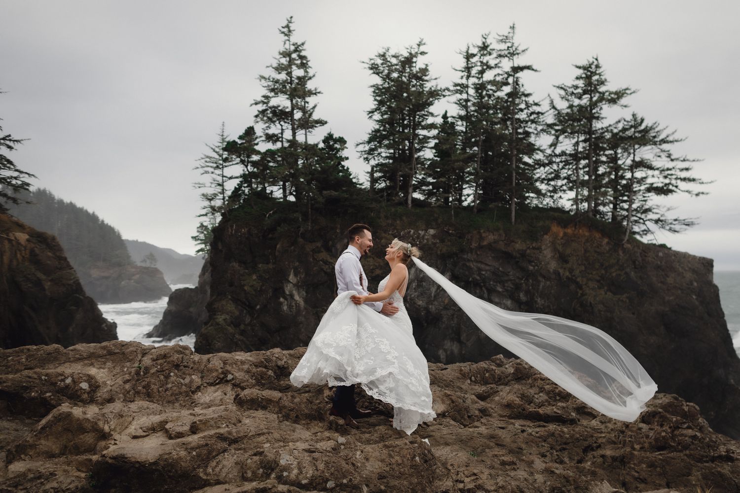 A romantic dip pose on rocky cliffs with a windswept veil and ocean backdrop.