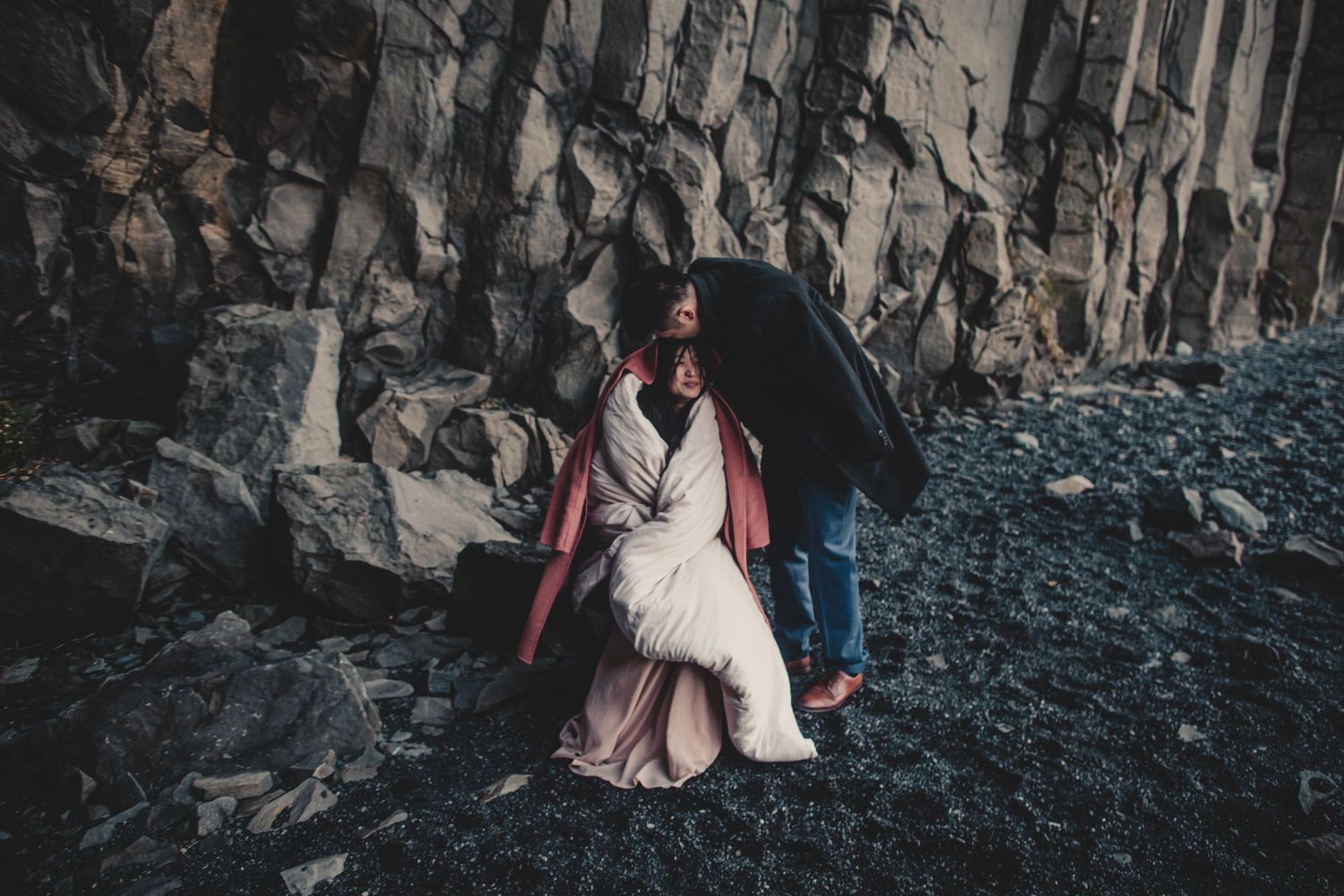 An intimate moment captured against rugged basalt cliffs on a rocky beach.