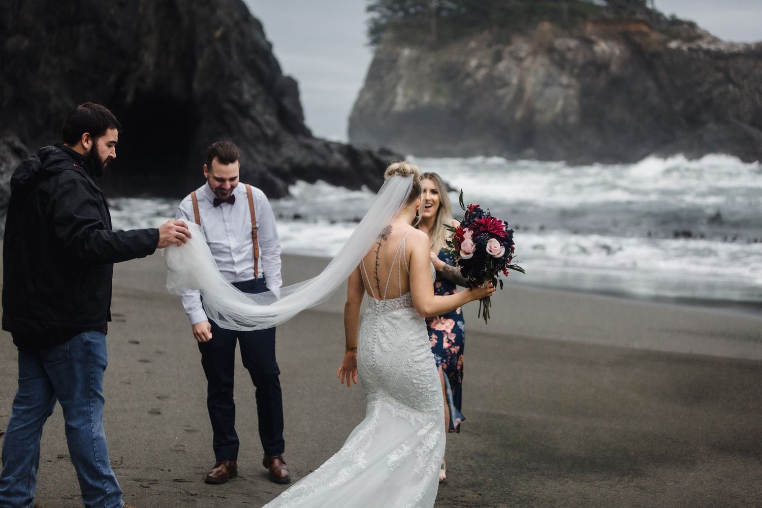 A dramatic wedding photoshoot on a moody beach with crashing waves and rocky cliffs in the background.